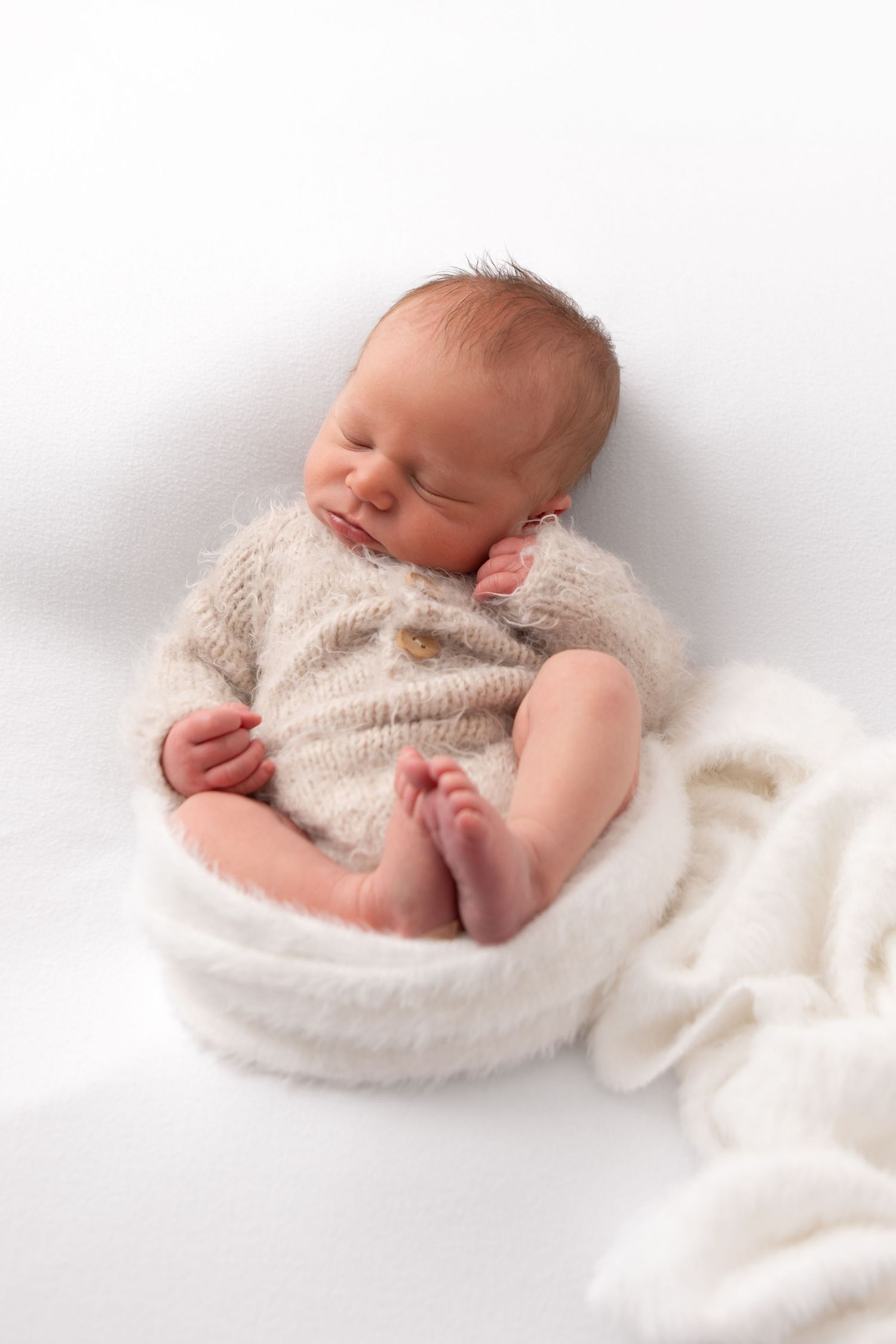 Sleeping newborn baby in beige knit romper on white blanket.