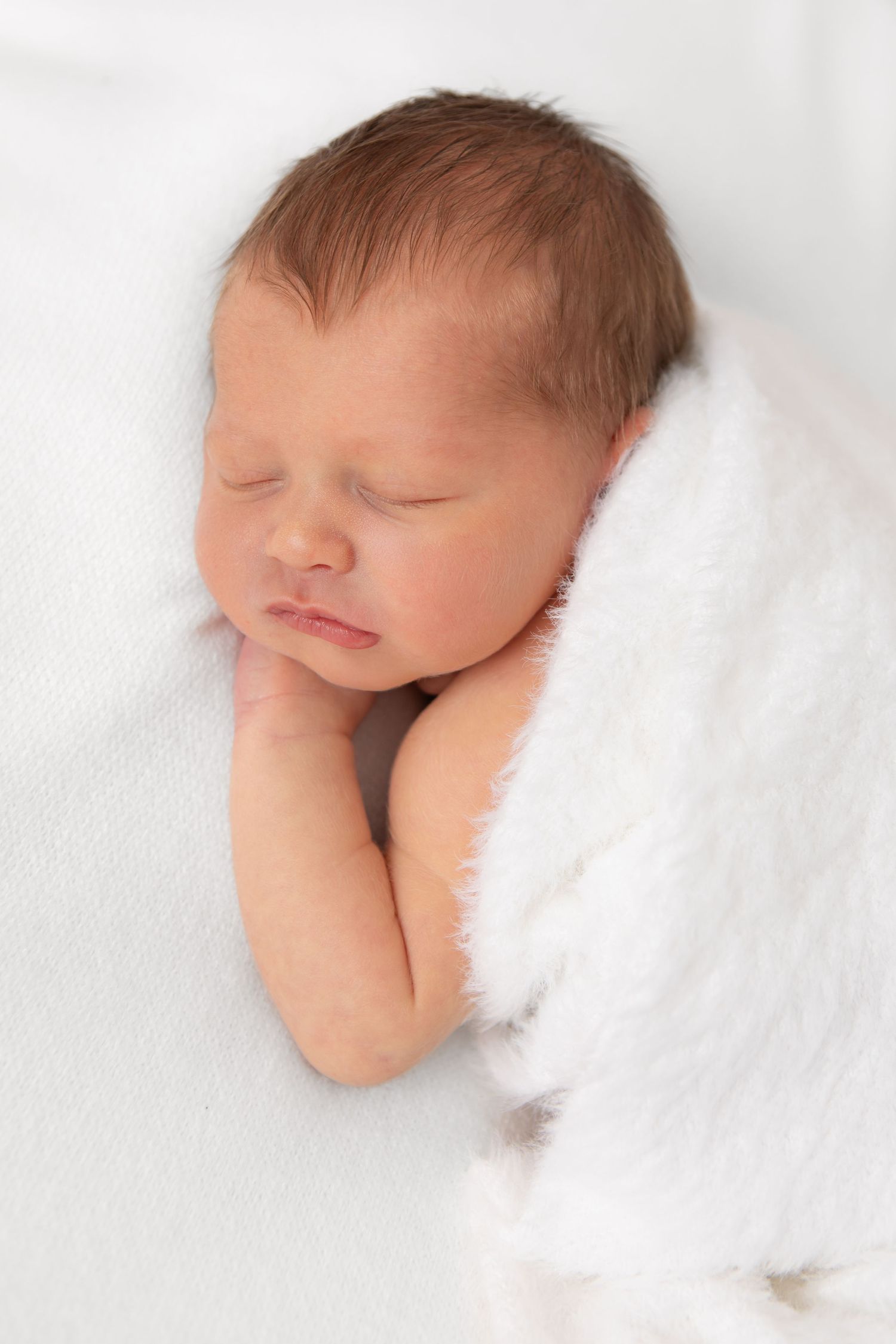 Close-up of newborn baby partially covered in soft white textured blanket.