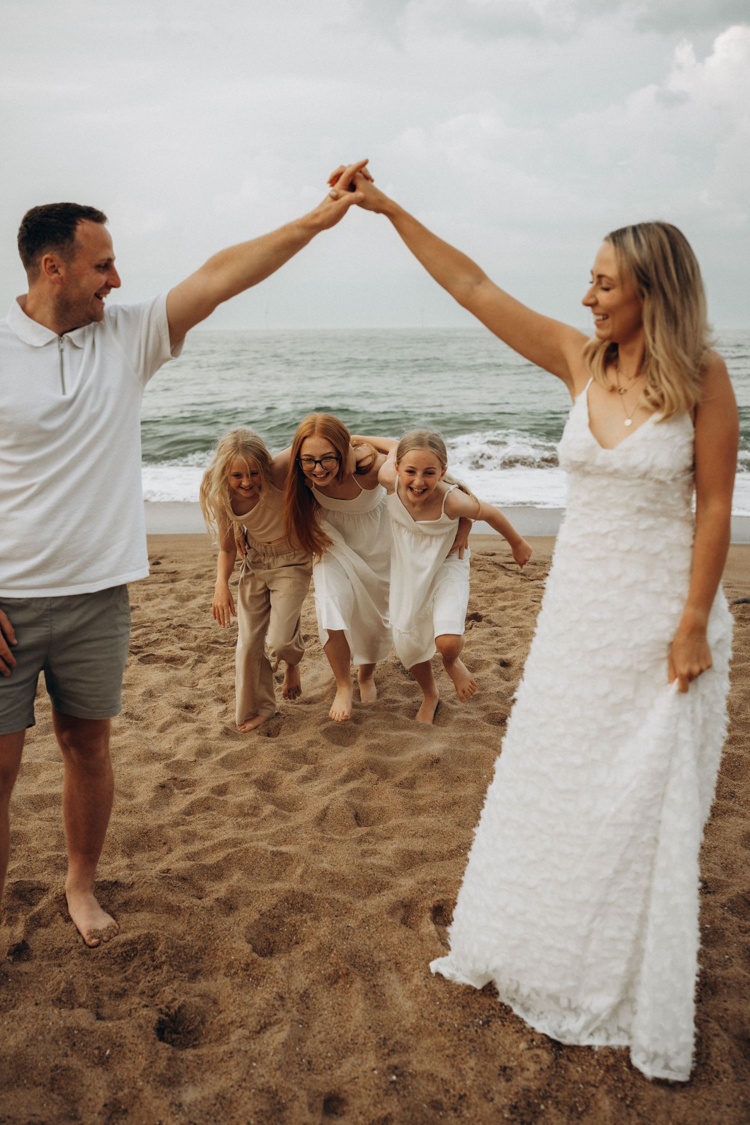 A family creates an archway with their arms while celebrating on the beach.