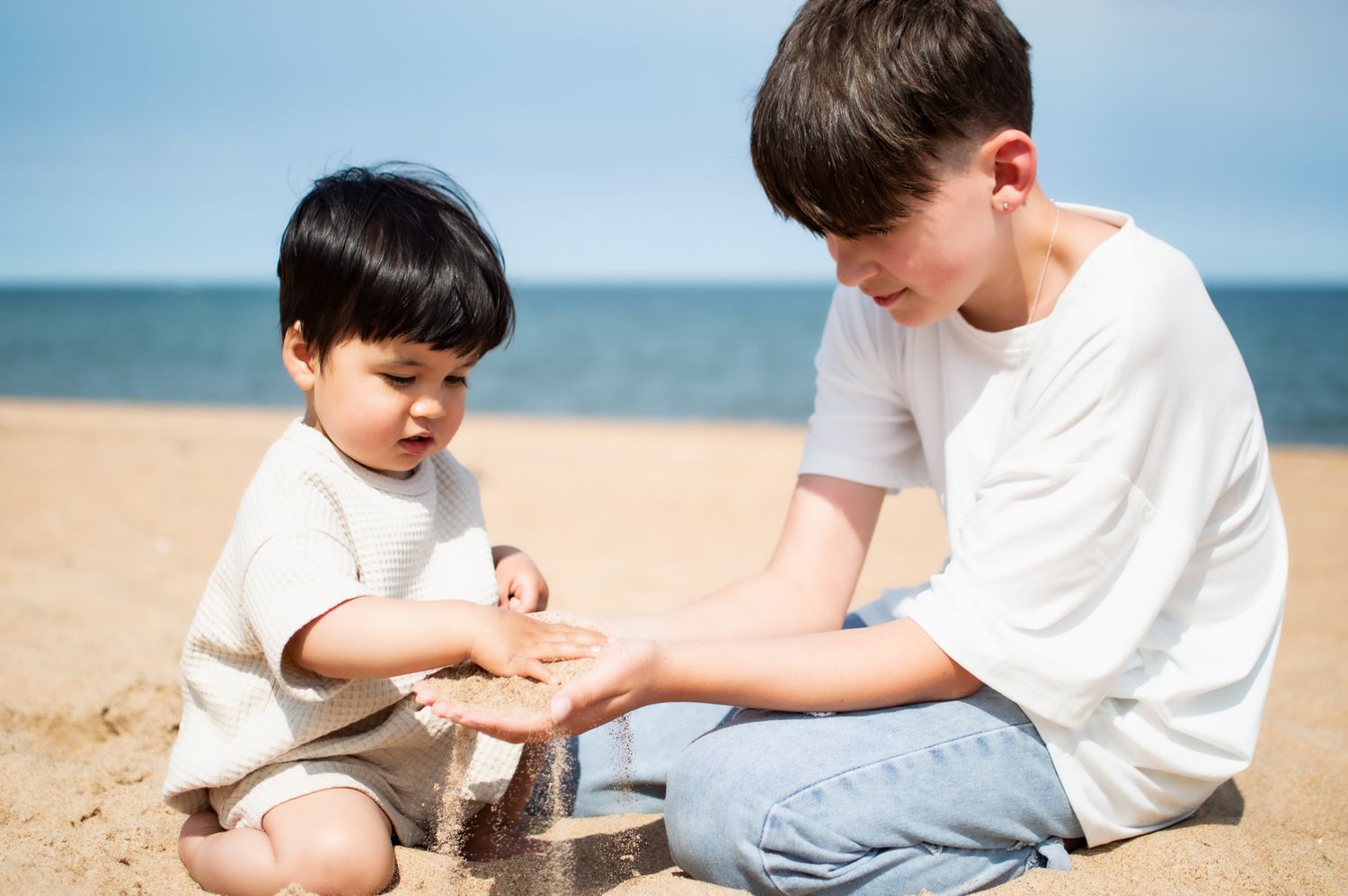 Young boy and toddler play together with sand on a sunny beach by the ocean.