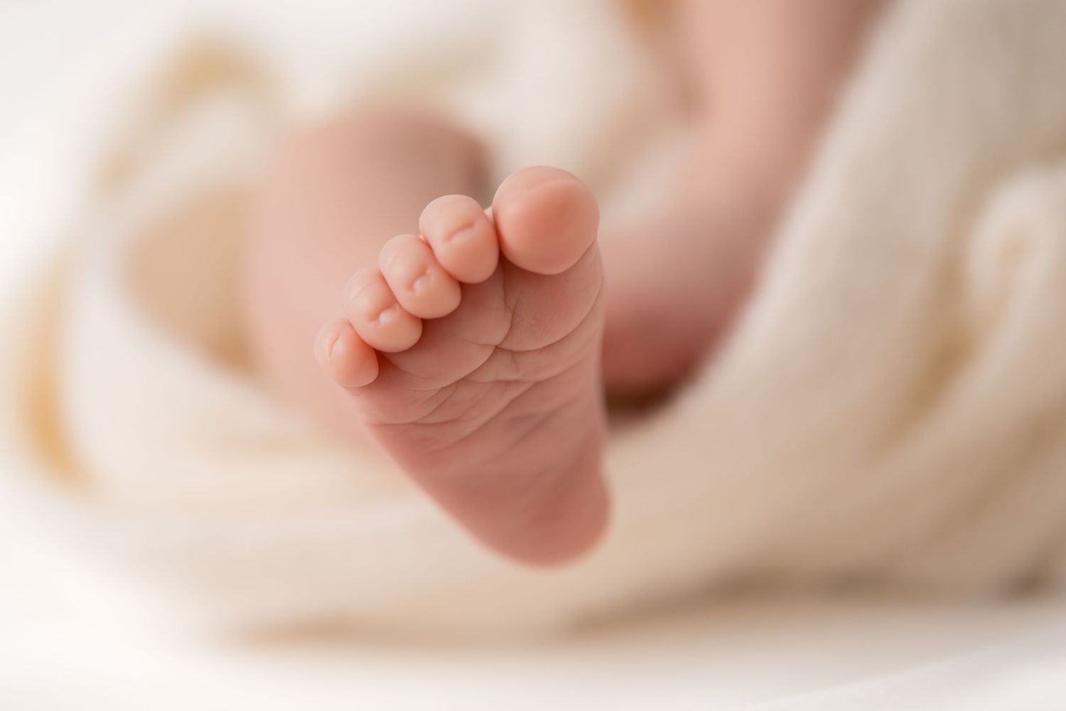 Delicate baby feet resting on white blanket in natural light.