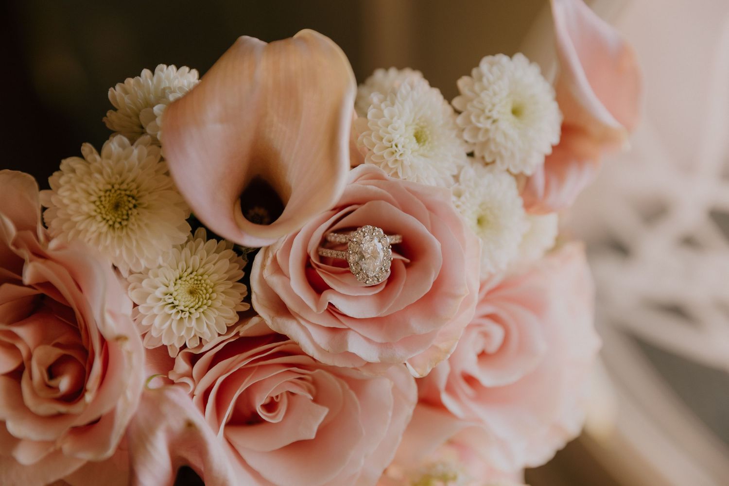 Pink roses and calla lilies bridal bouquet with a diamond engagement ring nestled among white chrysanthemums.
