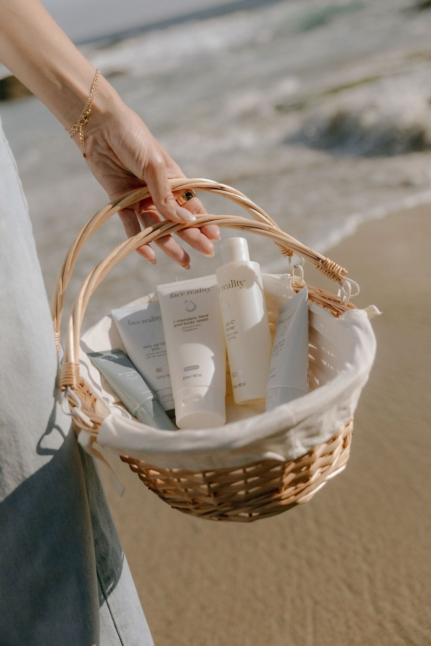 Woman holding a wicker basket with white skincare products on a sunny beach.