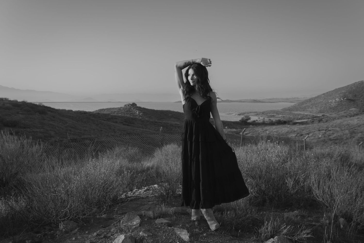 Silhouette of person in dress standing in grassy field during sunset.