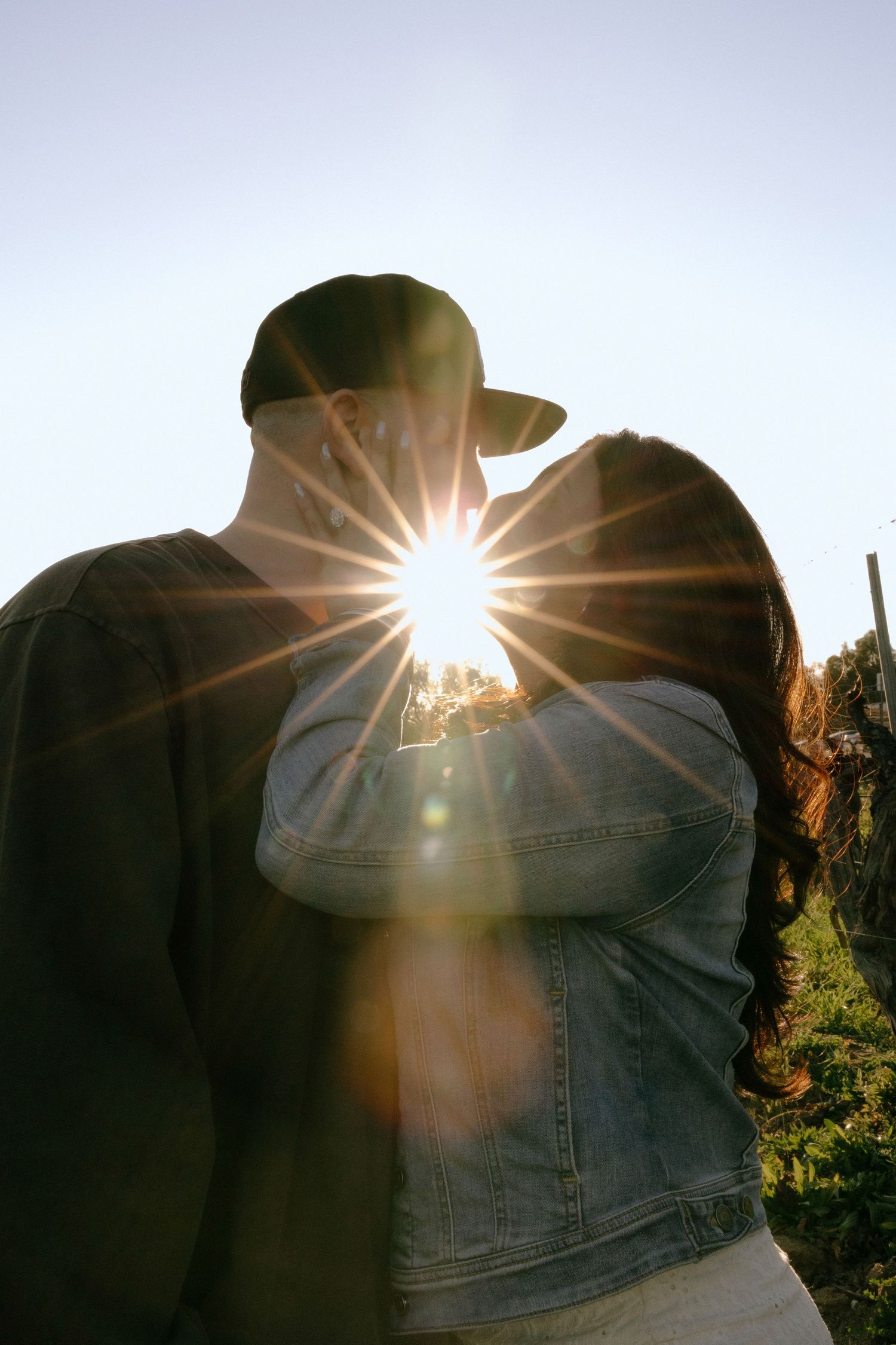 Two silhouettes embrace in a romantic sunset moment with sun flares creating a dreamy backlit effect.