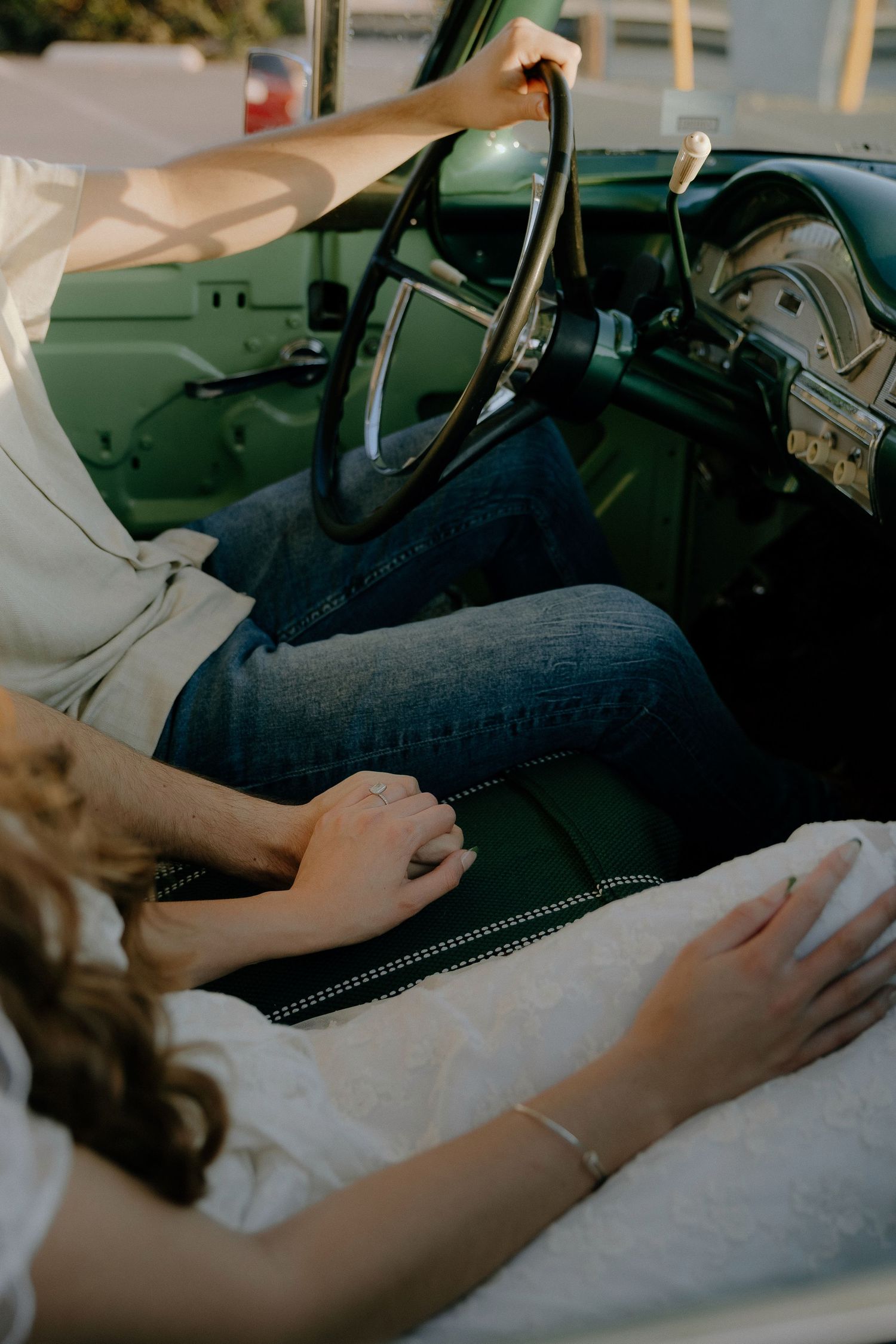 Couple sitting in a vintage green car, holding hands on the seat, wearing jeans and white tops.