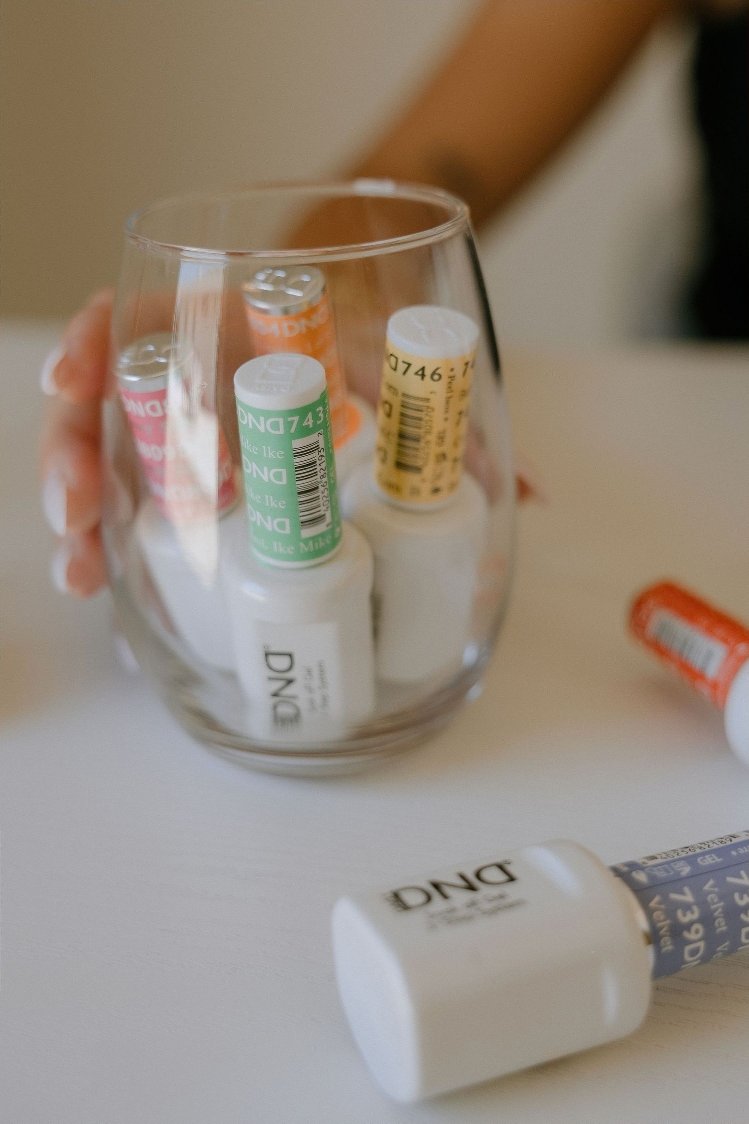 DND nail gel polish bottles stored in a clear stemless wine glass on a white table.