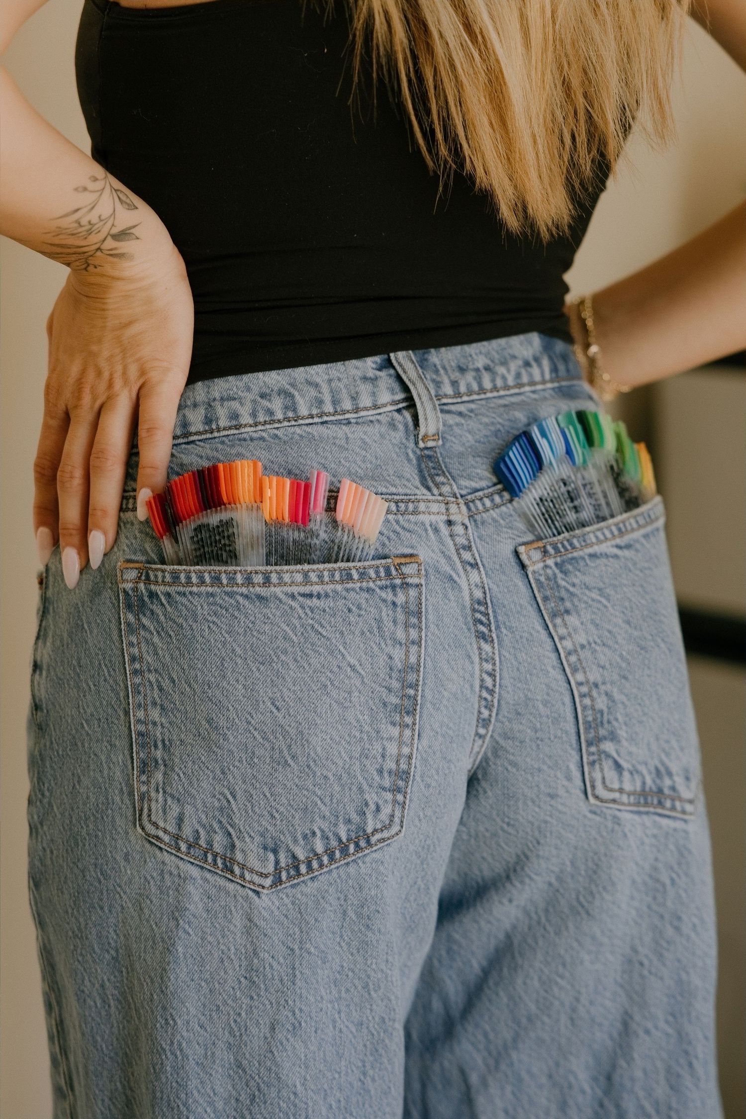 Woman in light wash jeans with colorful markers and pens stored in back pockets, wearing a black tank top.