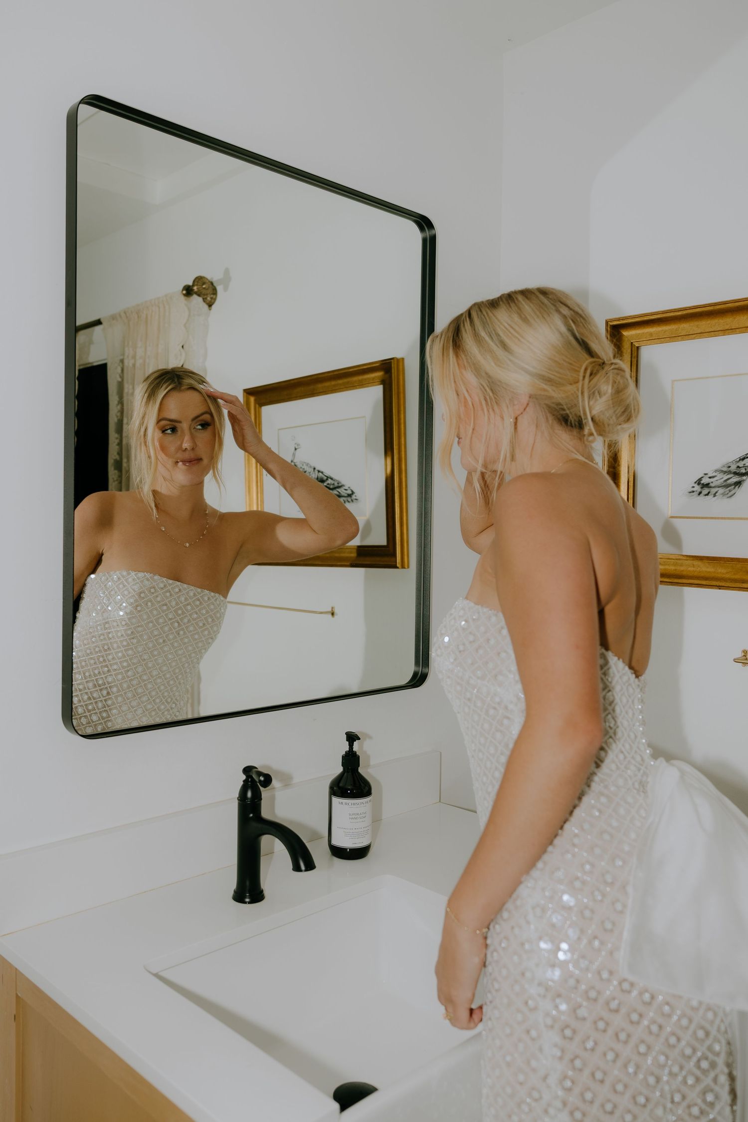 Person in white lace dress looking at reflection in bathroom mirror.
