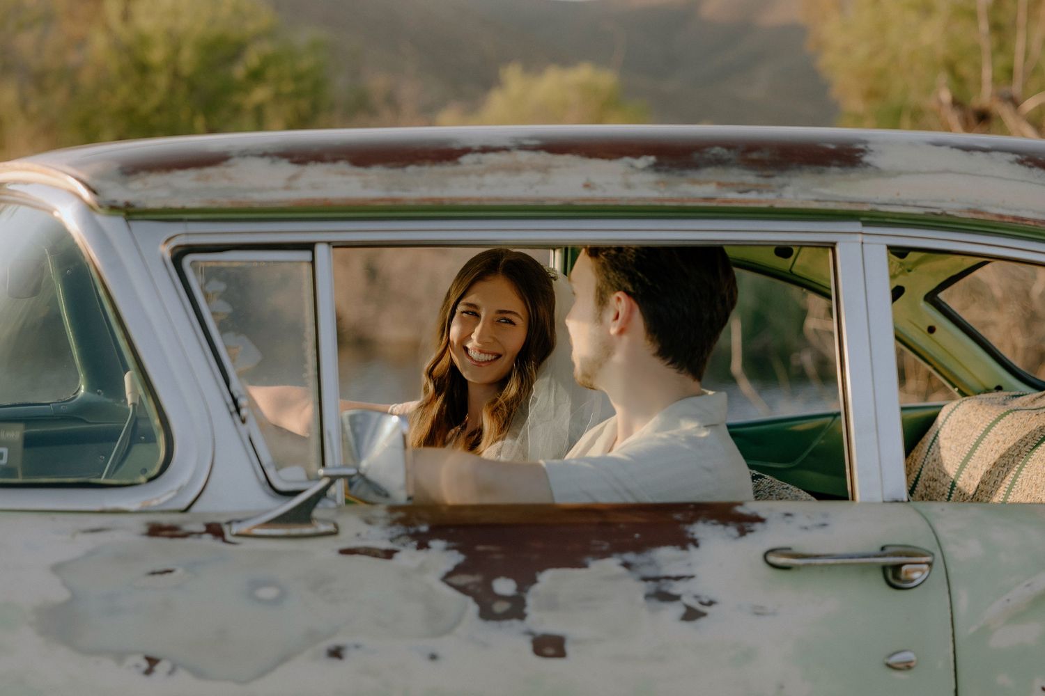 Couple sharing a romantic moment inside a vintage rustic car during golden hour outdoor engagement session.