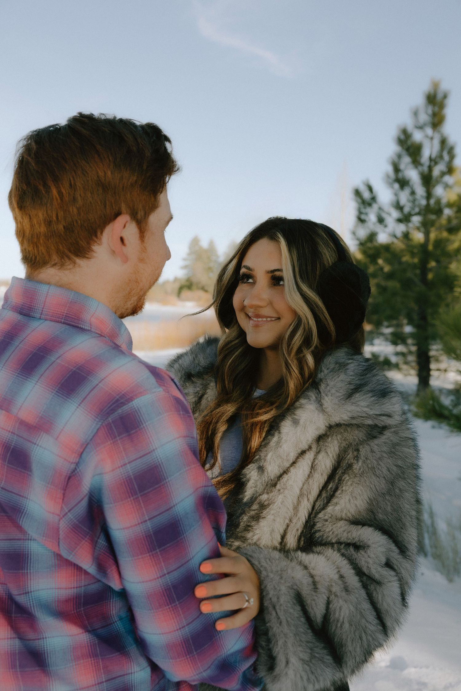 A couple shares an intimate winter moment outdoors, with one wearing a plaid shirt and the other in a fur coat.