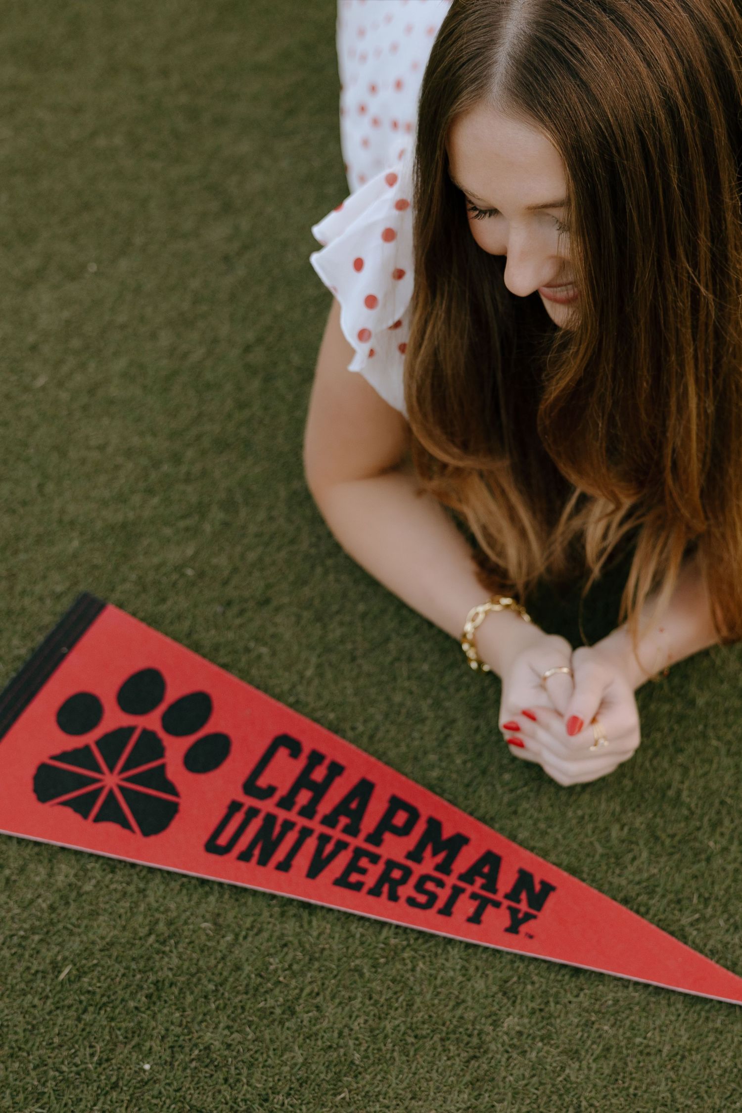 Young woman lying on grass looking at a red Chapman University pennant with paw print logo.
