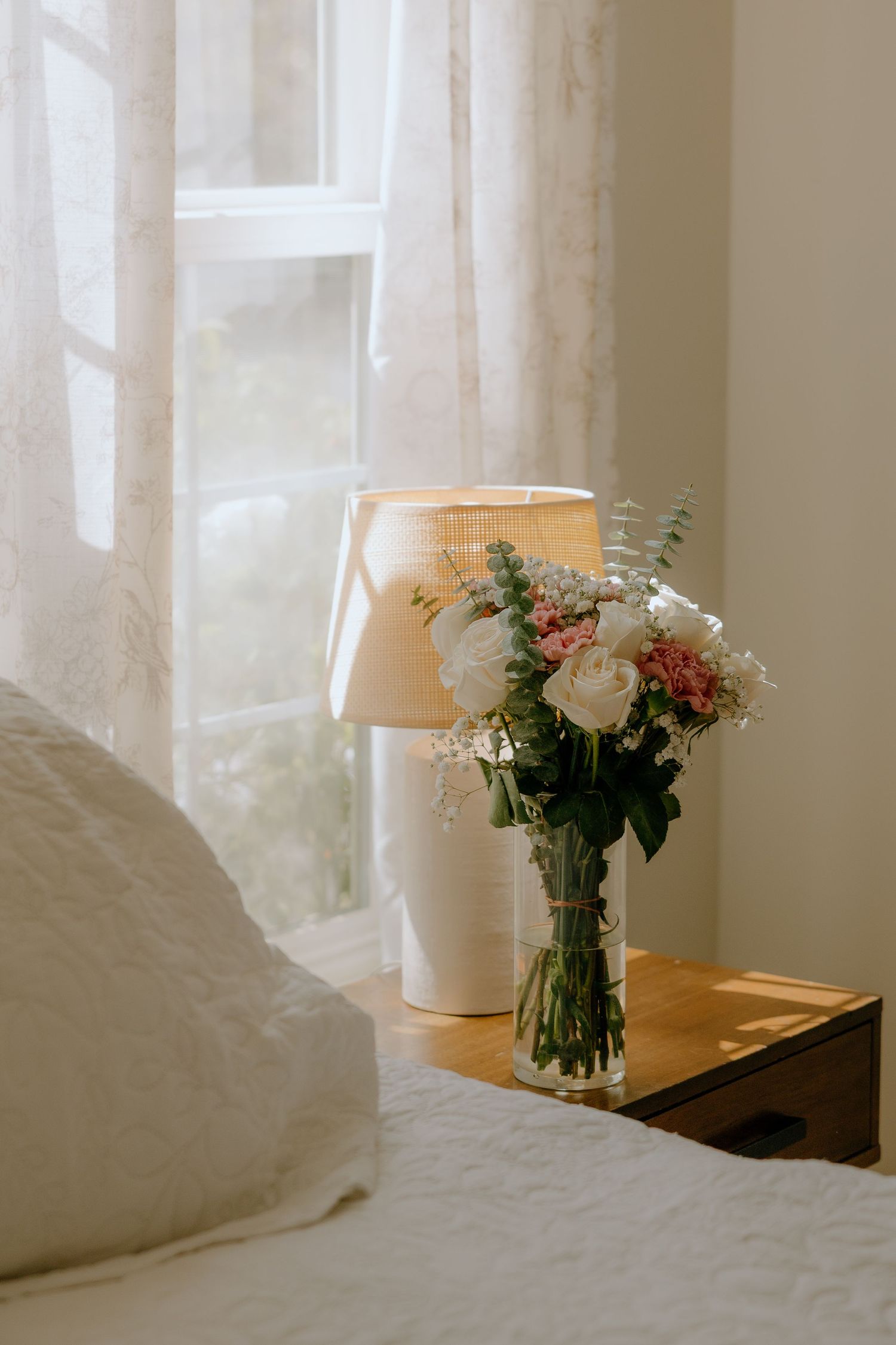 Elegant white roses and flowers in a vase by a sunlit window with sheer curtains.