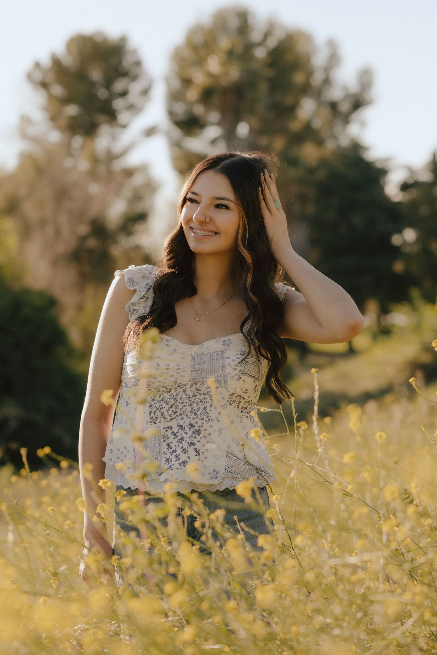 Person in white lace top poses gracefully in golden wildflower field during sunset.