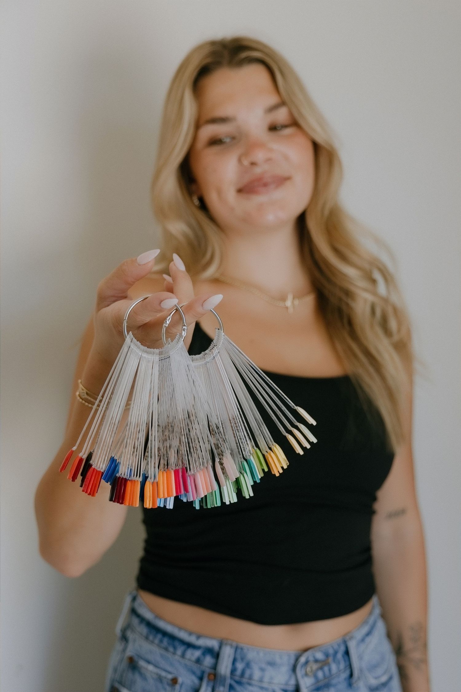 Smiling blonde woman holding a colorful nail polish swatch ring fan display with multiple shades.