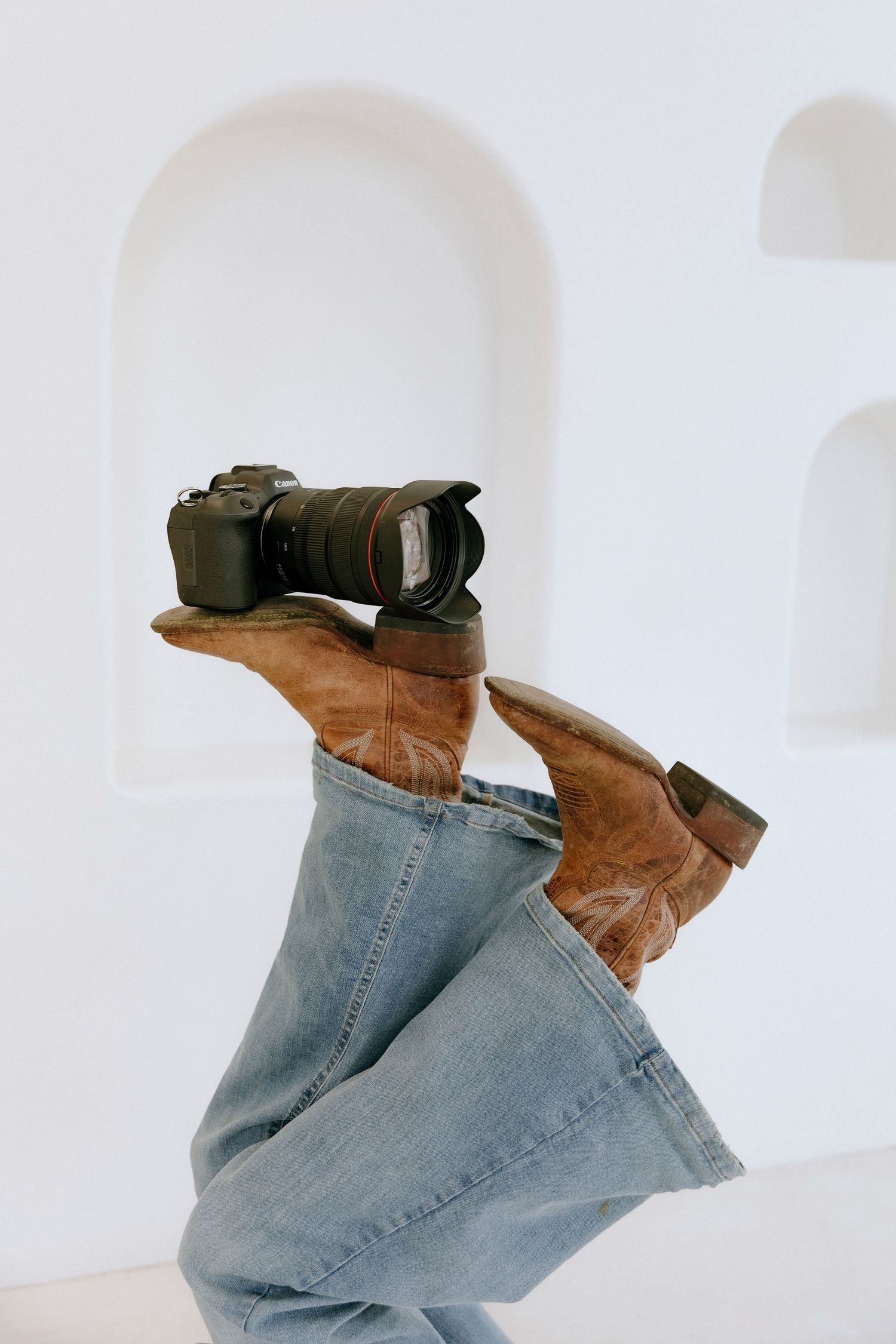 A pair of brown leather boots and light blue jeans photographed in a minimalist white setting.