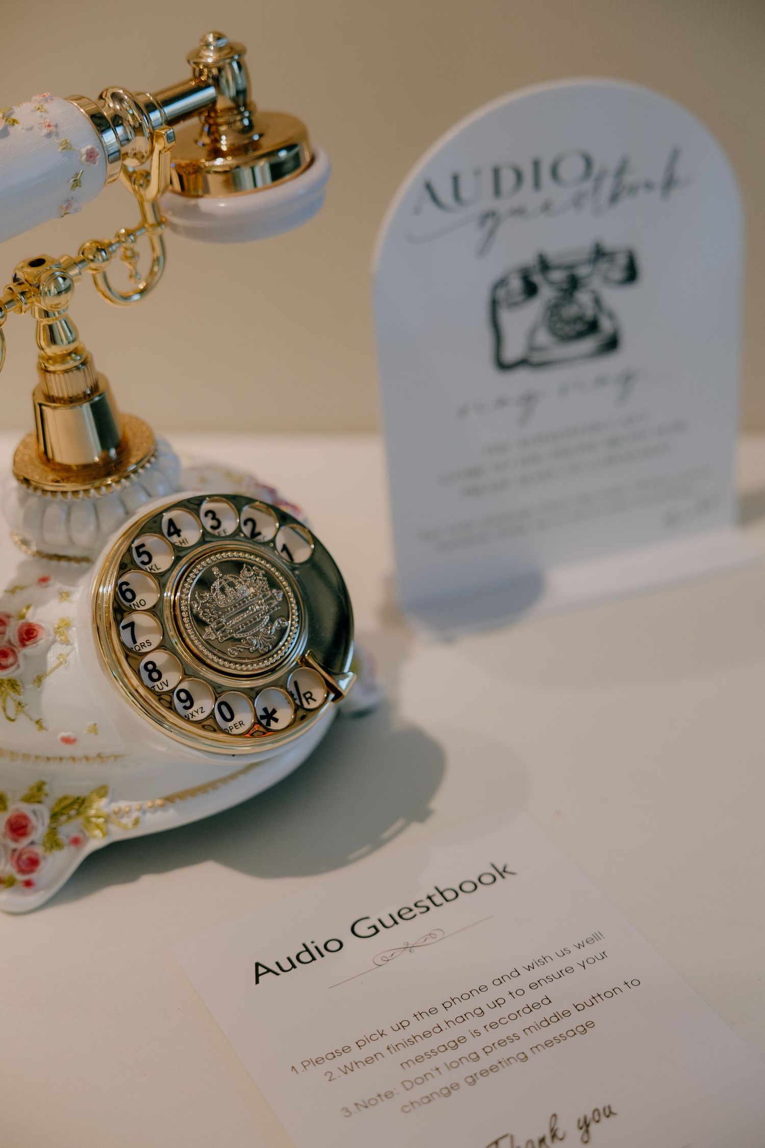 Vintage floral rotary phone audio guestbook display at a wedding reception with elegant gold accents.