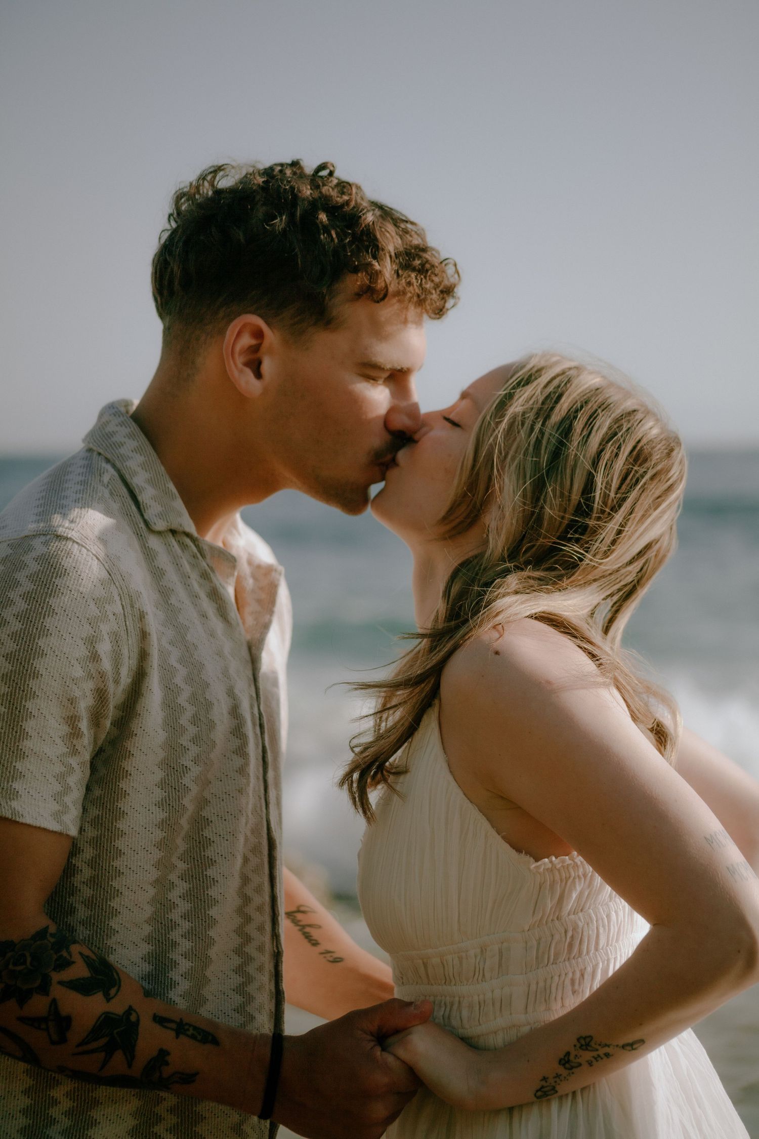 A couple embraces romantically on a beach at sunset with the ocean waves in the background.