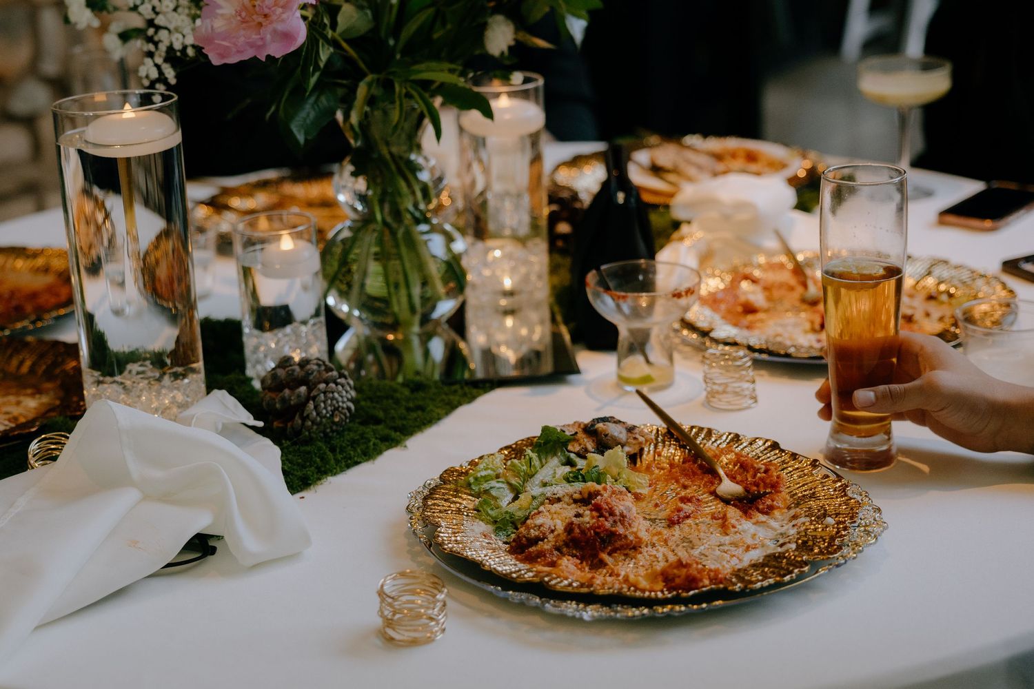 Elegant wedding reception table with lit candles, floral centerpiece, salad dish, and drinks in soft ambient lighting.