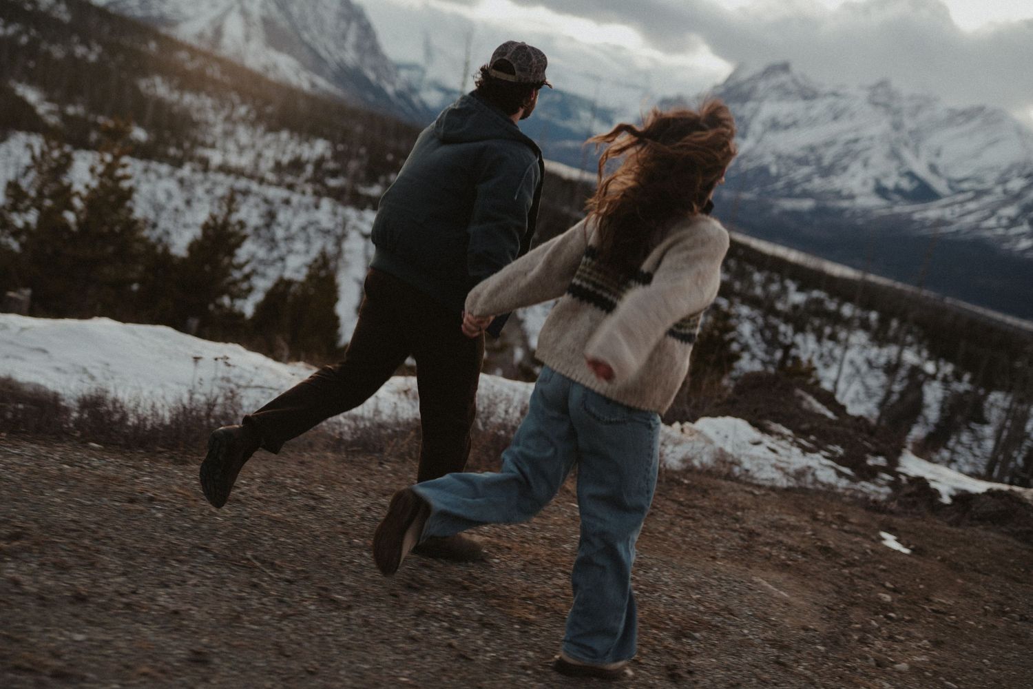 A couple embracing and running through a snowy, mountainous landscape.