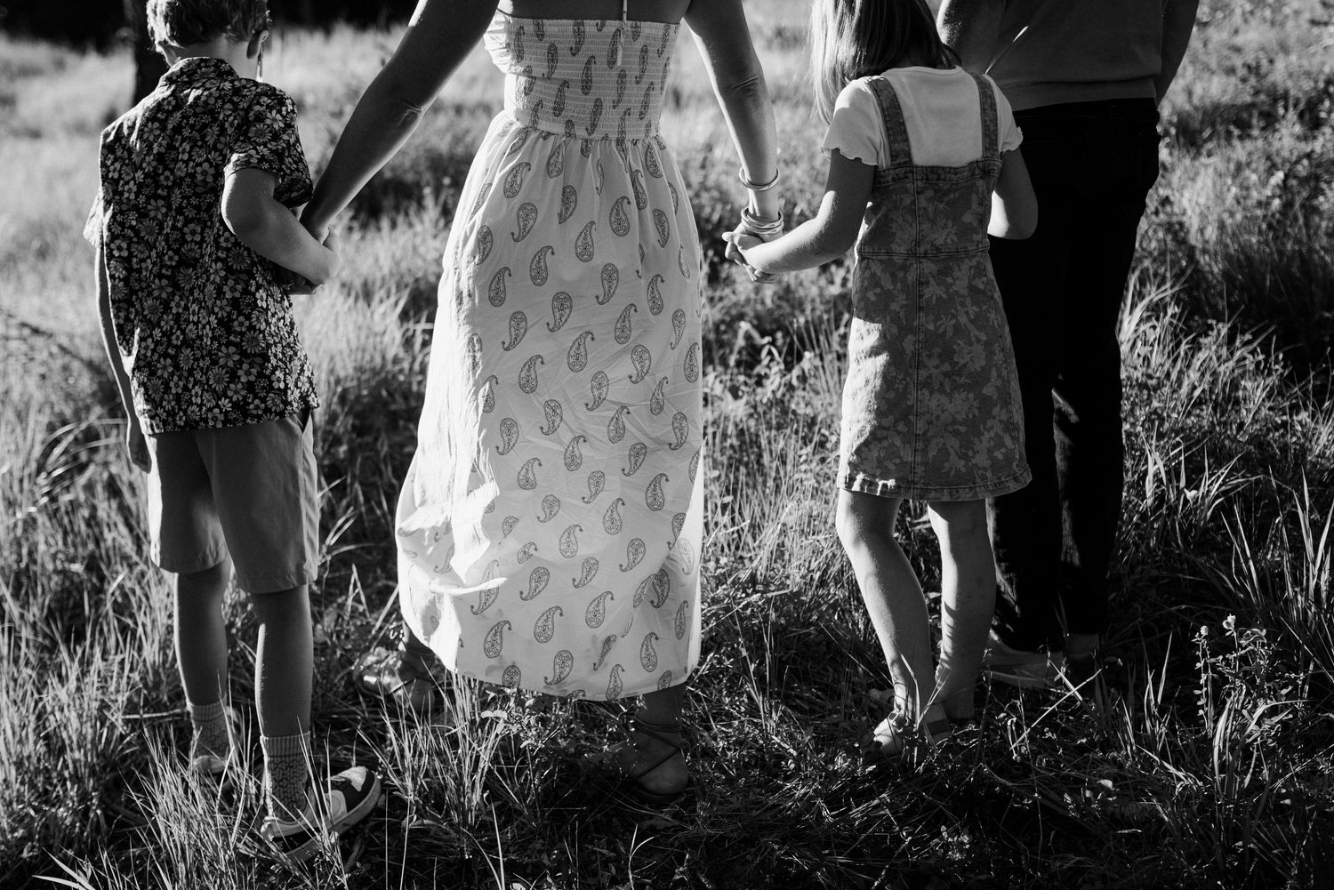 A group of people in casual summer clothing walk together through tall grass in a black and white photograph.