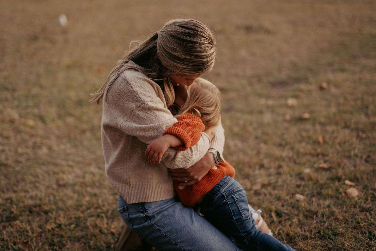 Two people share an intimate embrace on a grassy field during golden hour.