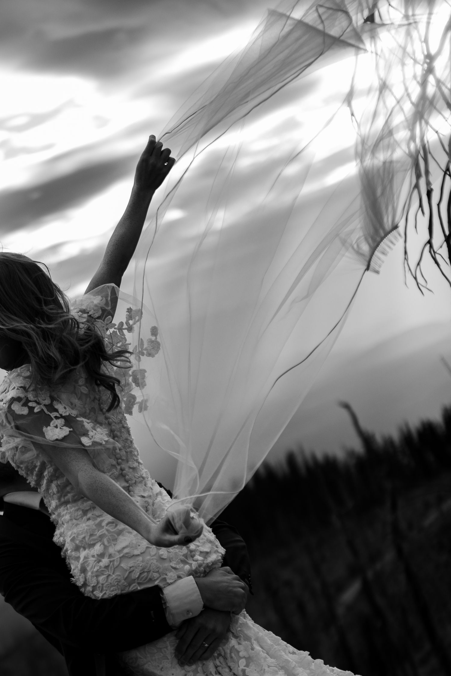 A dramatic black and white photo shows a flowing wedding veil caught in the wind against a moody sky.
