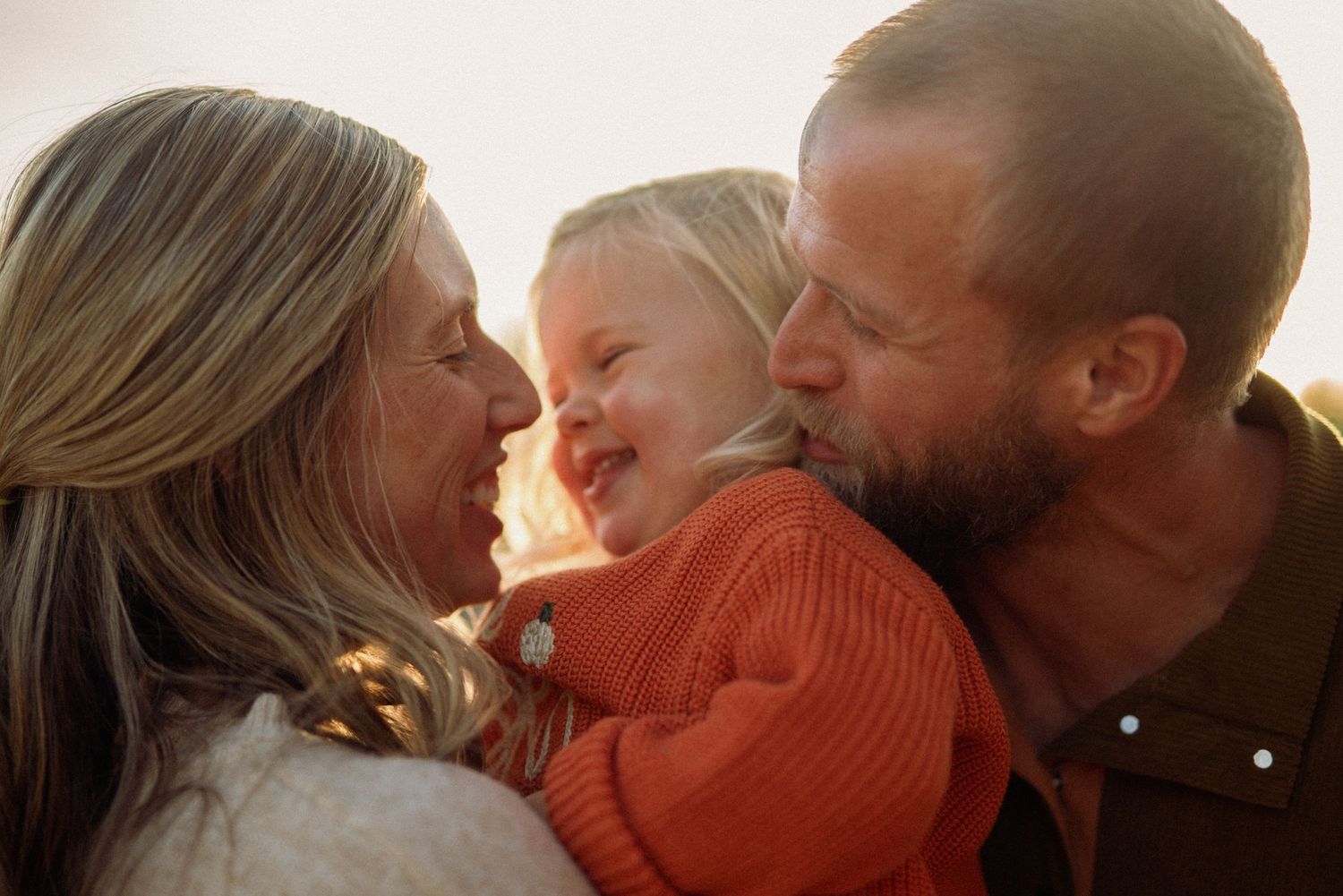 Parents and their toddler share a tender moment in warm lighting while wearing warm clothing.
