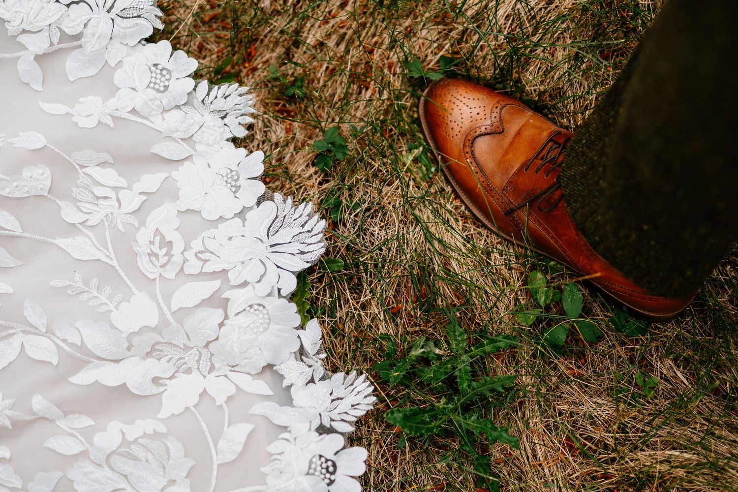 White wedding dress train and groom's shoe on grassy lawn.