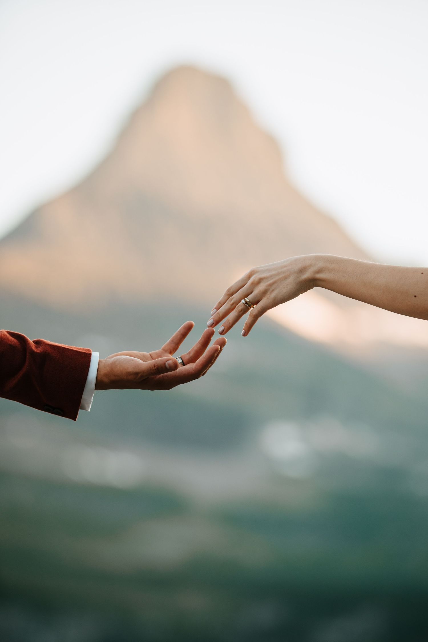 Two hands reaching out towards each other in a serene mountain landscape.