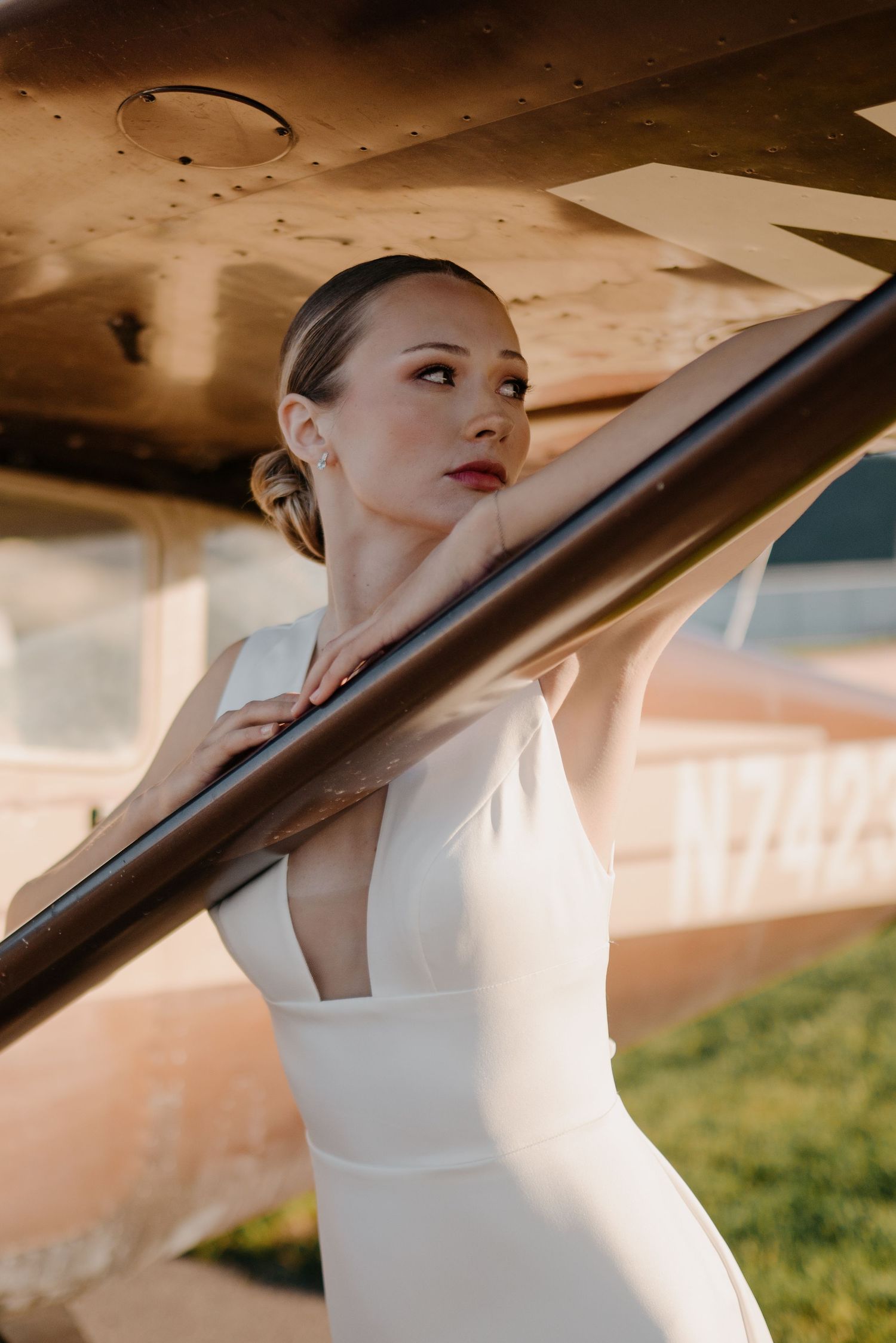 Artistic shots under an airplane wing in a white dress against a sunny backdrop.