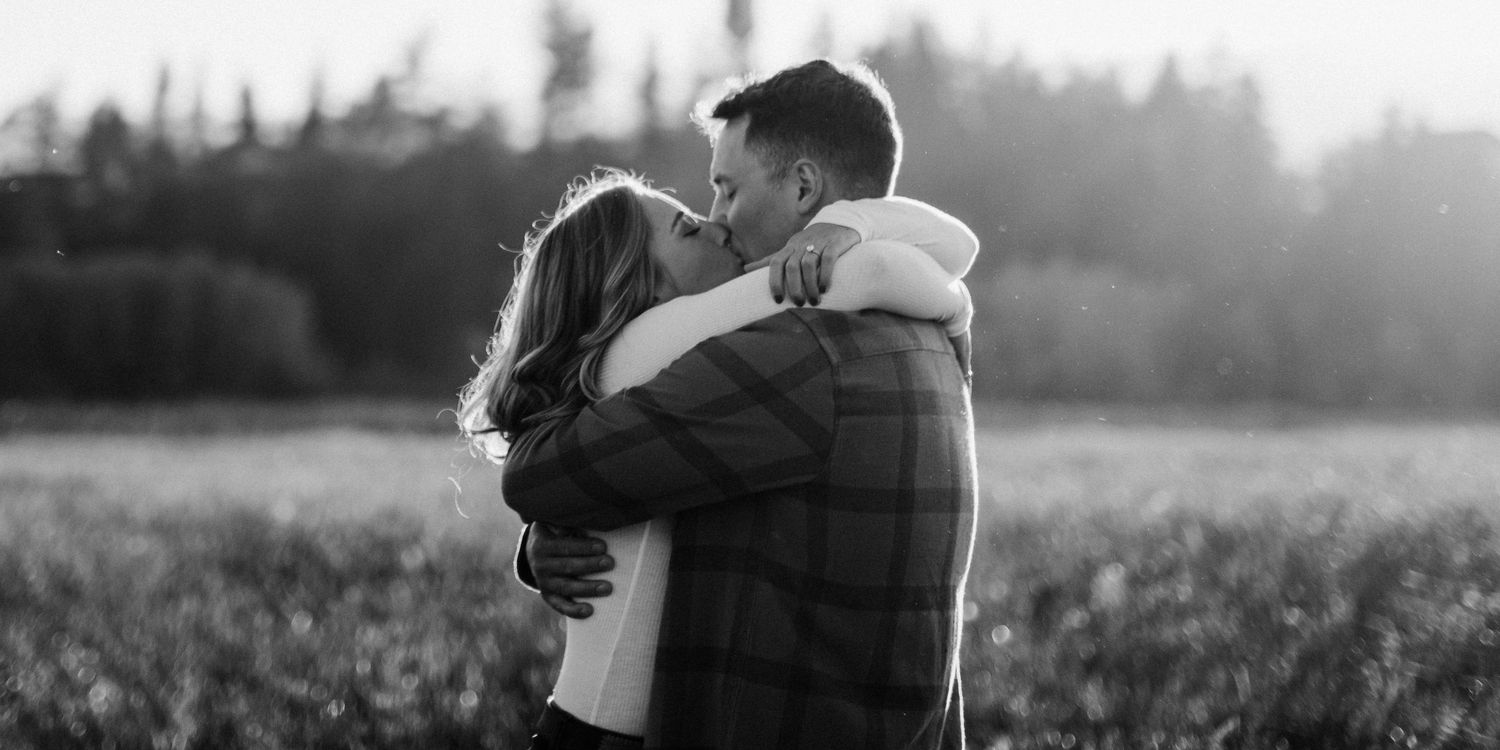 A romantic embrace captured in black and white in a rural field at dusk.