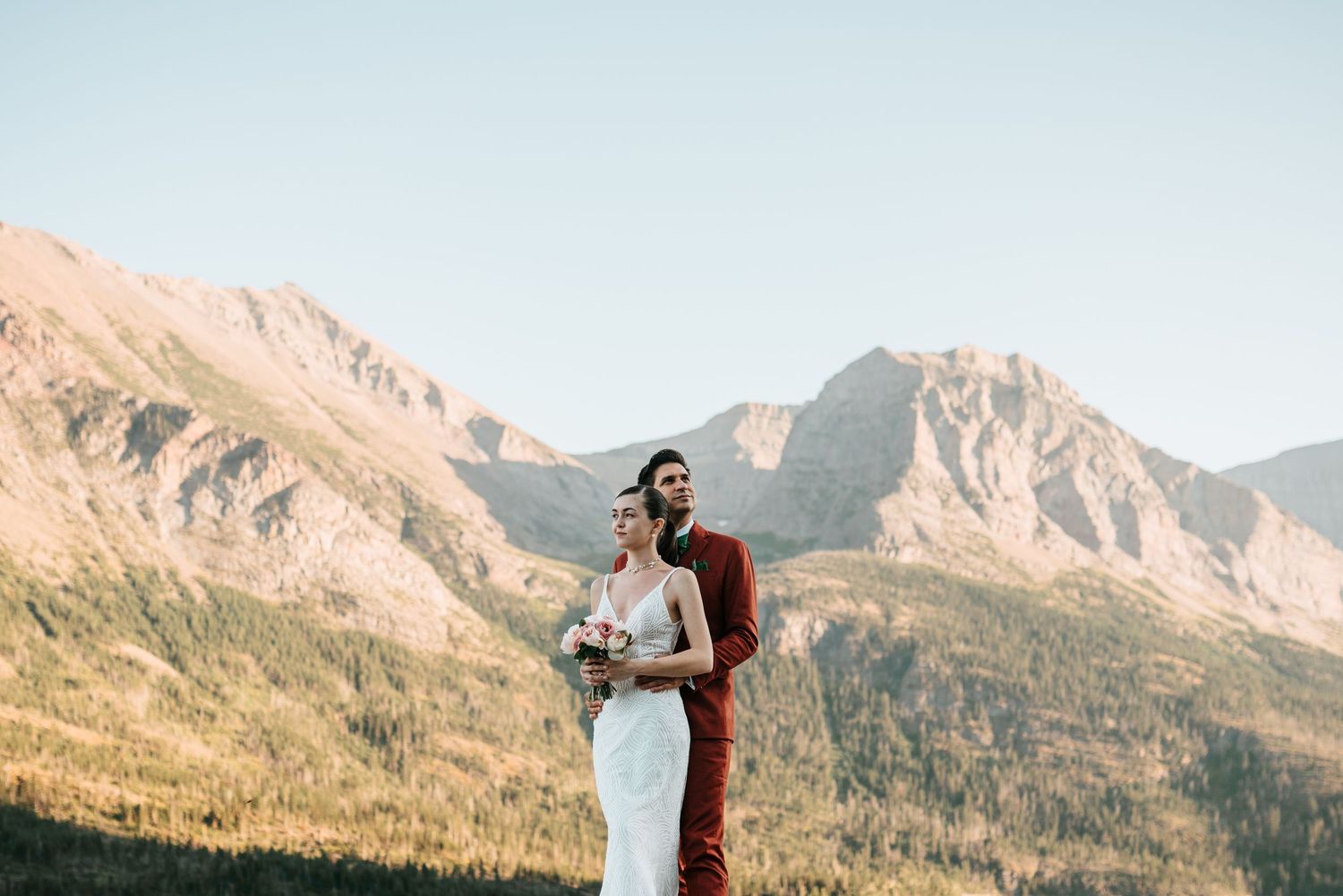 A bride and groom stand in front of a scenic mountain landscape on their wedding day.