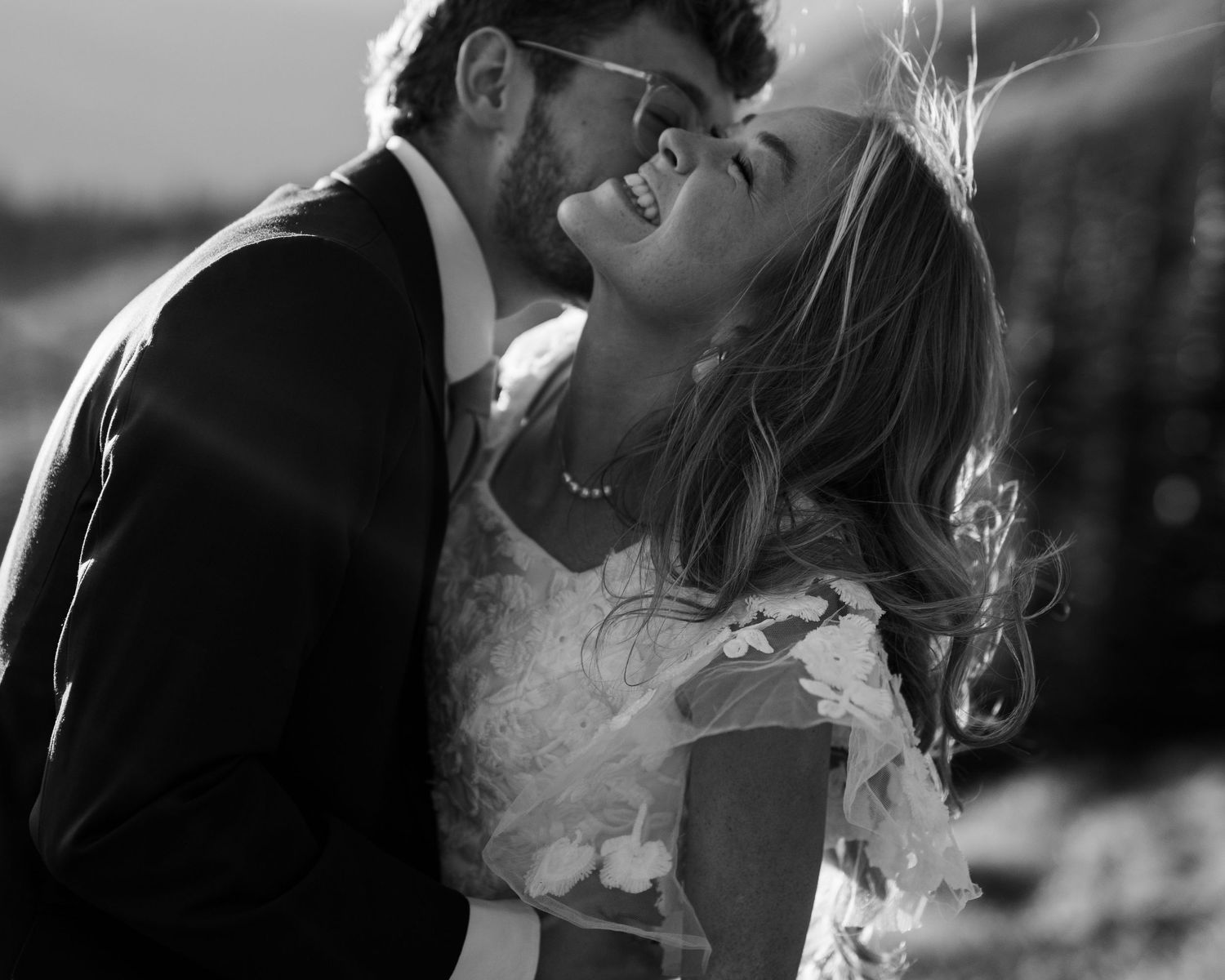 A romantic black and white wedding photo showing a tender moment between newlyweds in sunlight.