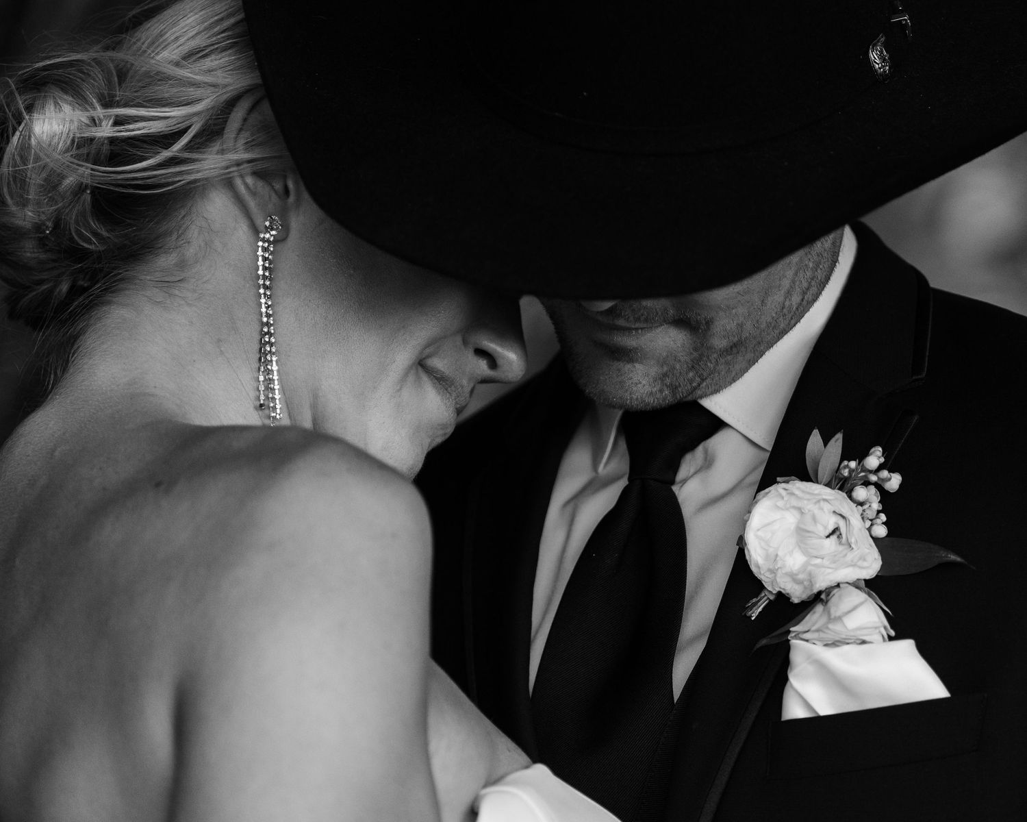 A black and white photograph of a bride and groom in an intimate embrace, with the groom's face partially obscured.