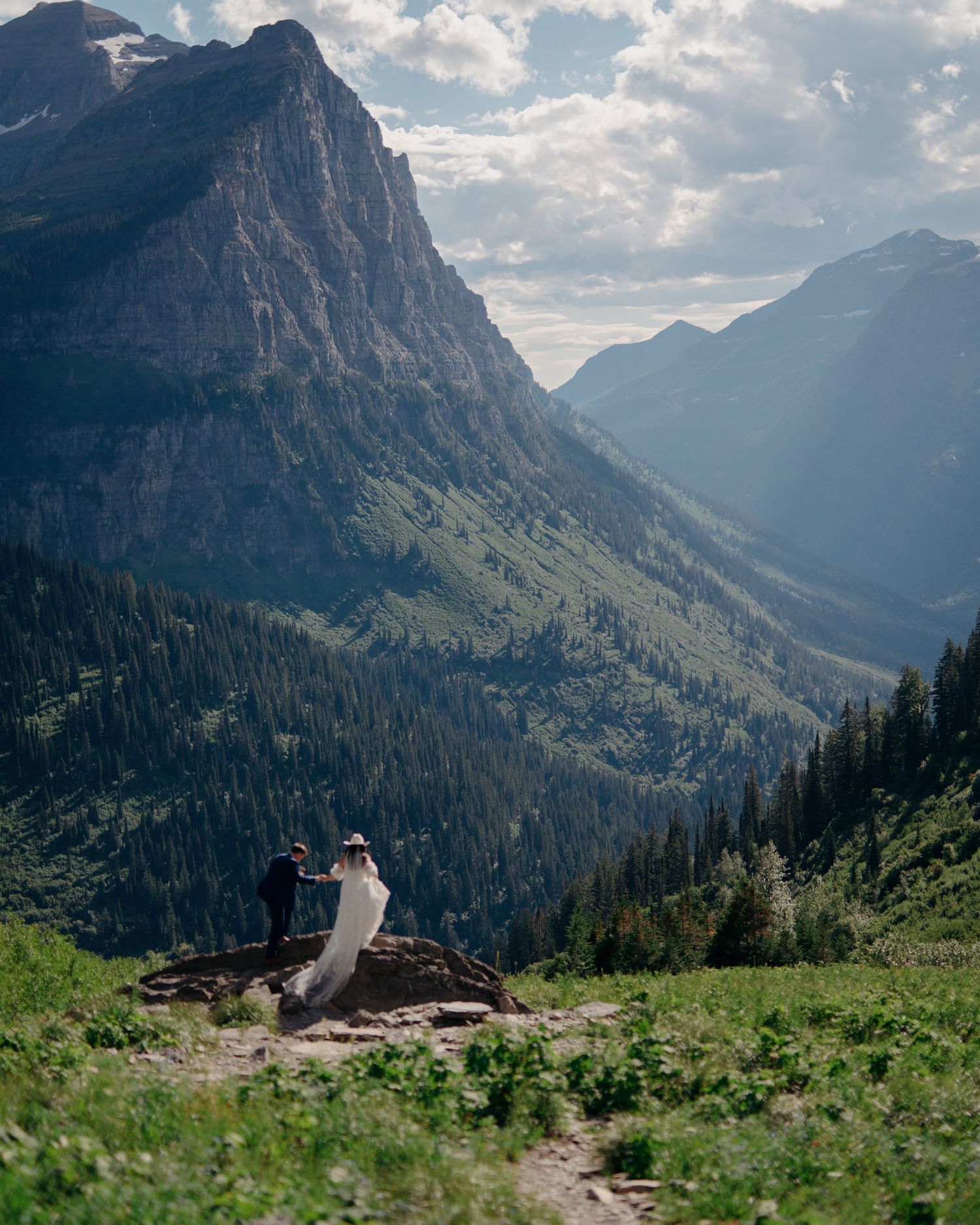 A scenic mountain landscape with a hiking trail and lush green vegetation in the foreground.