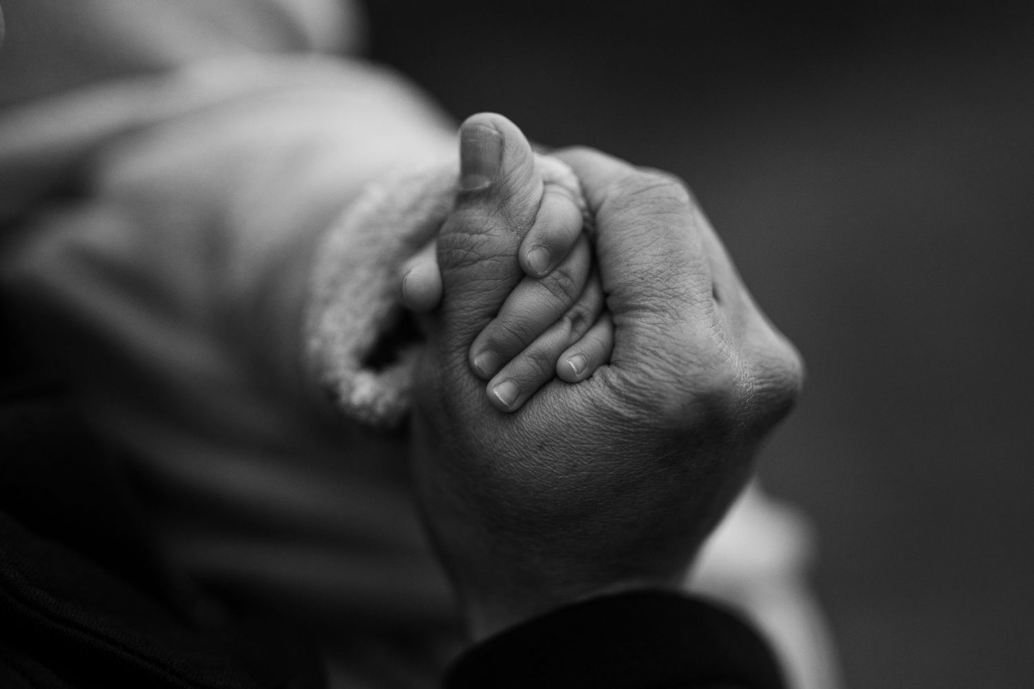 Black and white close-up photograph of two hands holding each other in a tender embrace.