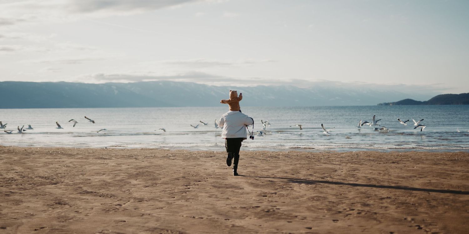 A person runs joyfully along a scenic beach while seagulls take flight against a backdrop of coastal cliffs and ocean.