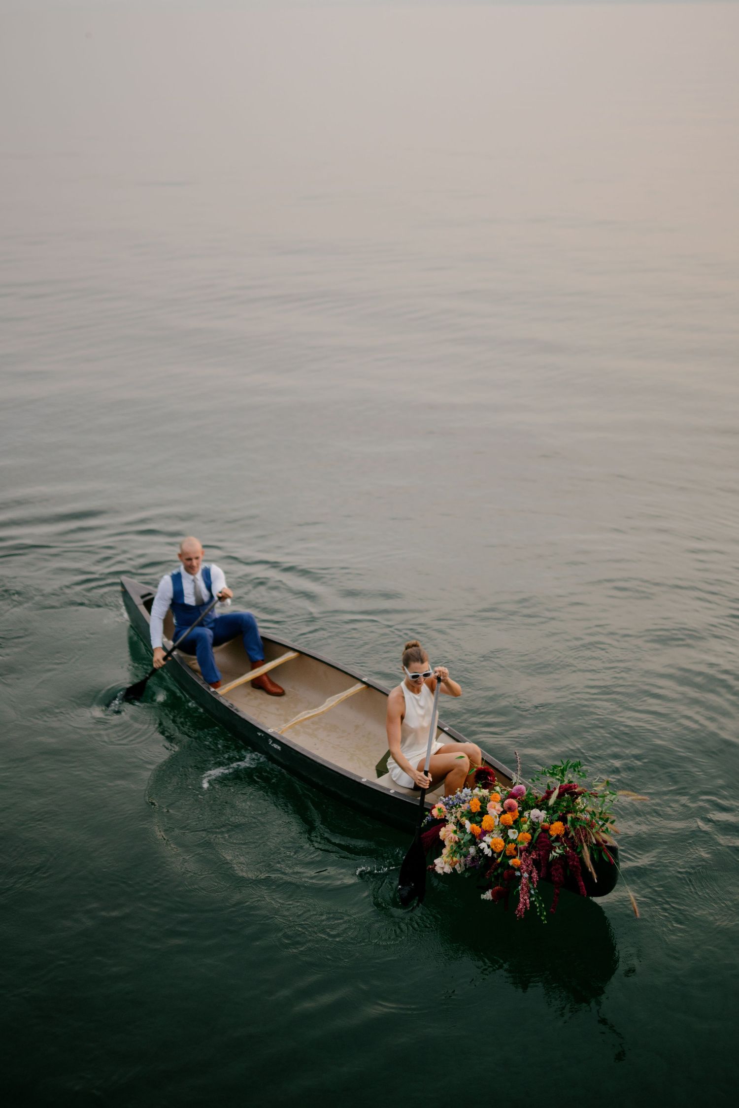 A person in a boat surrounded by flowers floats on a calm body of water.