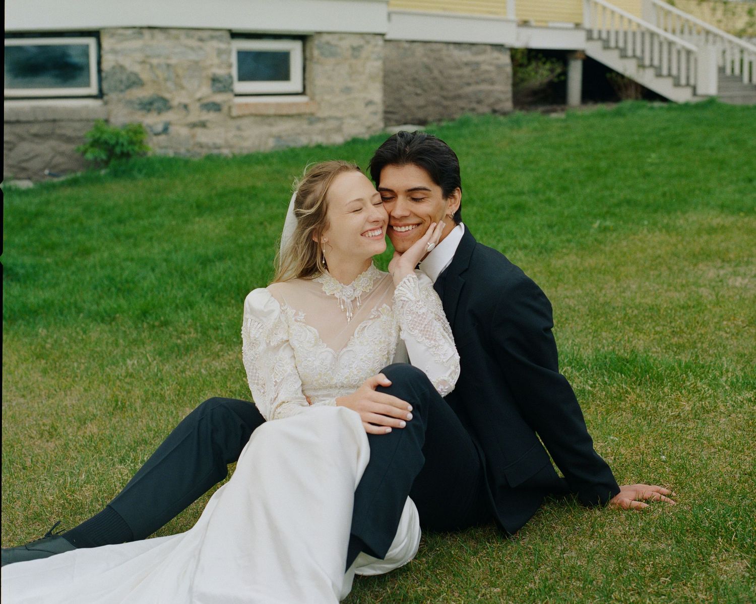 Bride and groom sitting together on green grass, sharing a romantic moment at outdoor wedding venue.