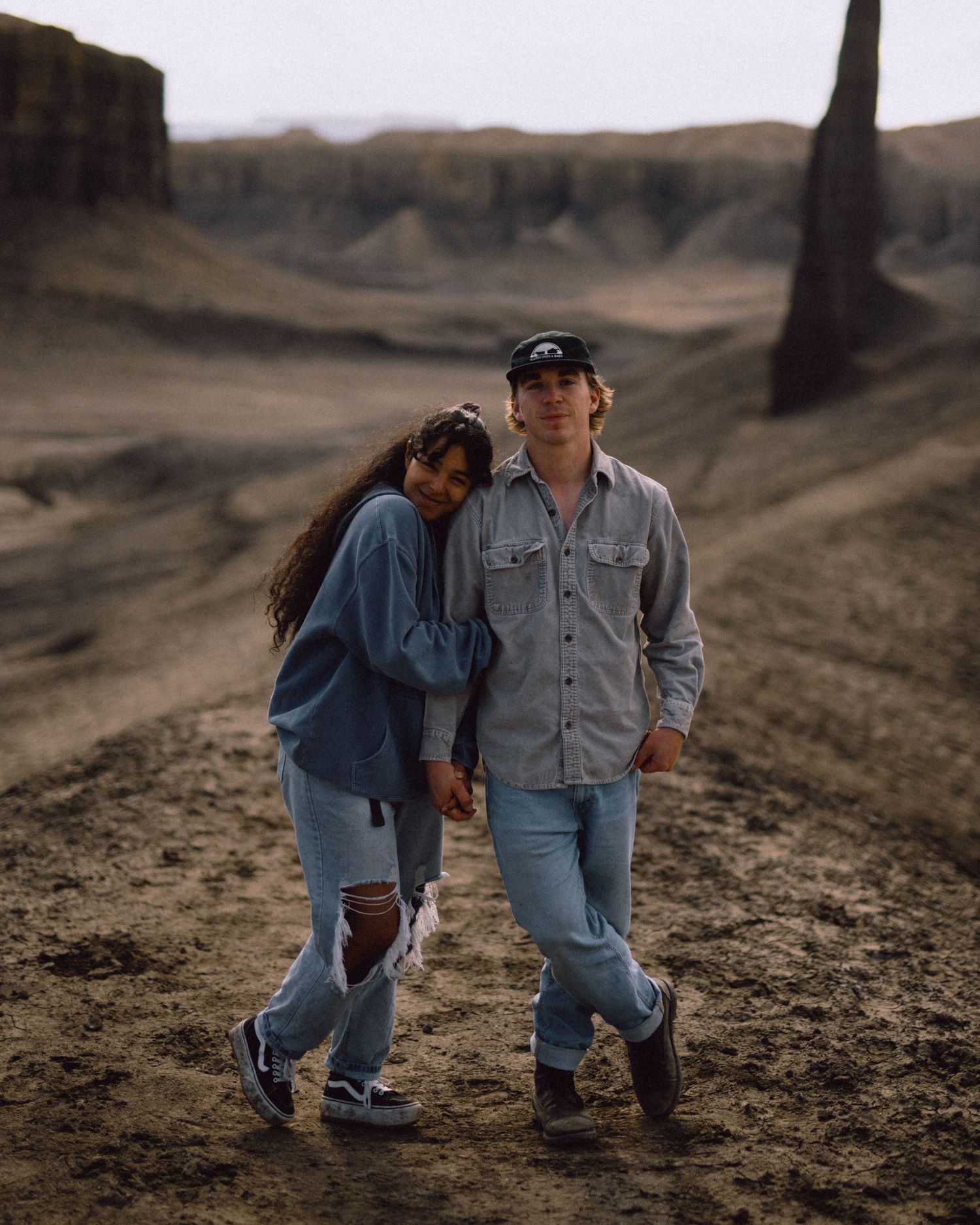 Couple in denim outfits walking together on rugged terrain at sunset.