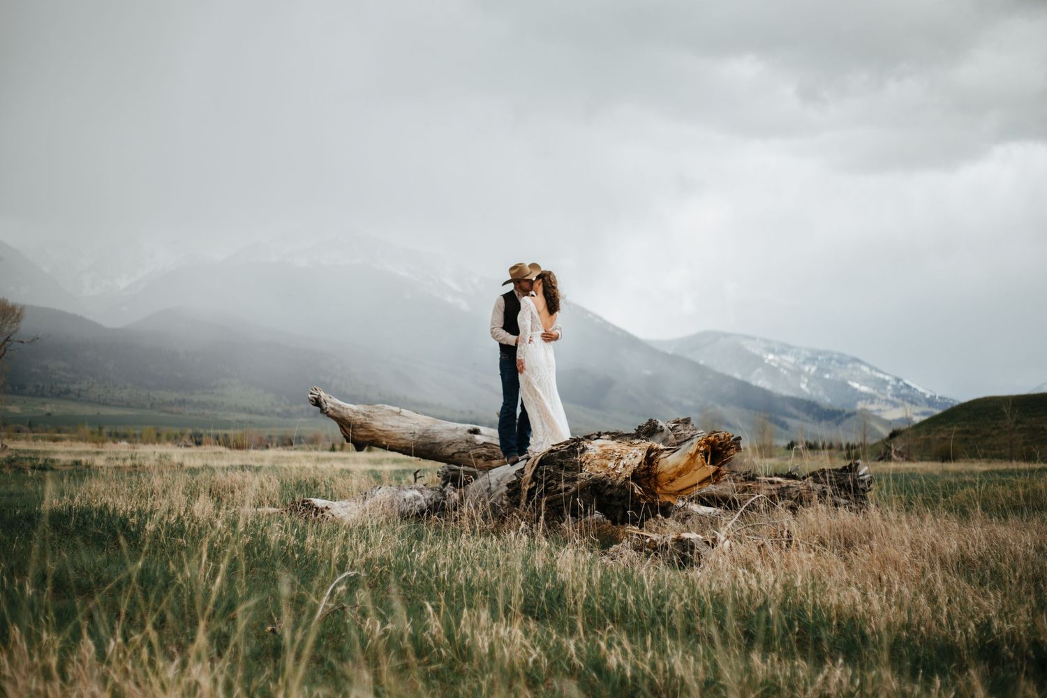 Eloping couple poses in dramatic mountain landscape with cloudy sky backdrop in Ennis, Montana.