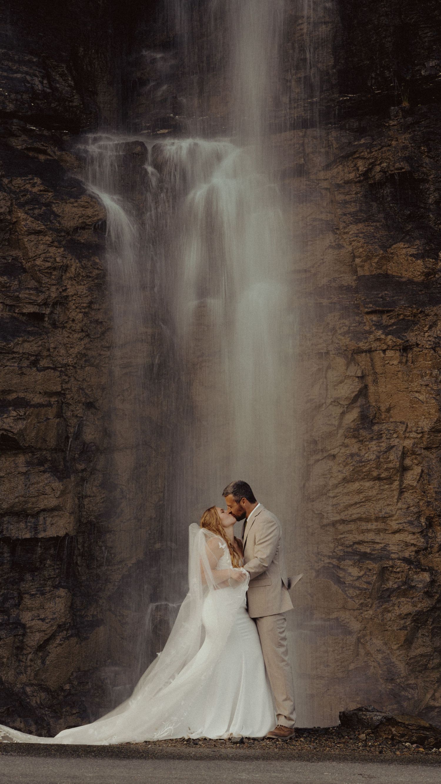 A couple embracing in front of a stunning waterfall surrounded by lush greenery.