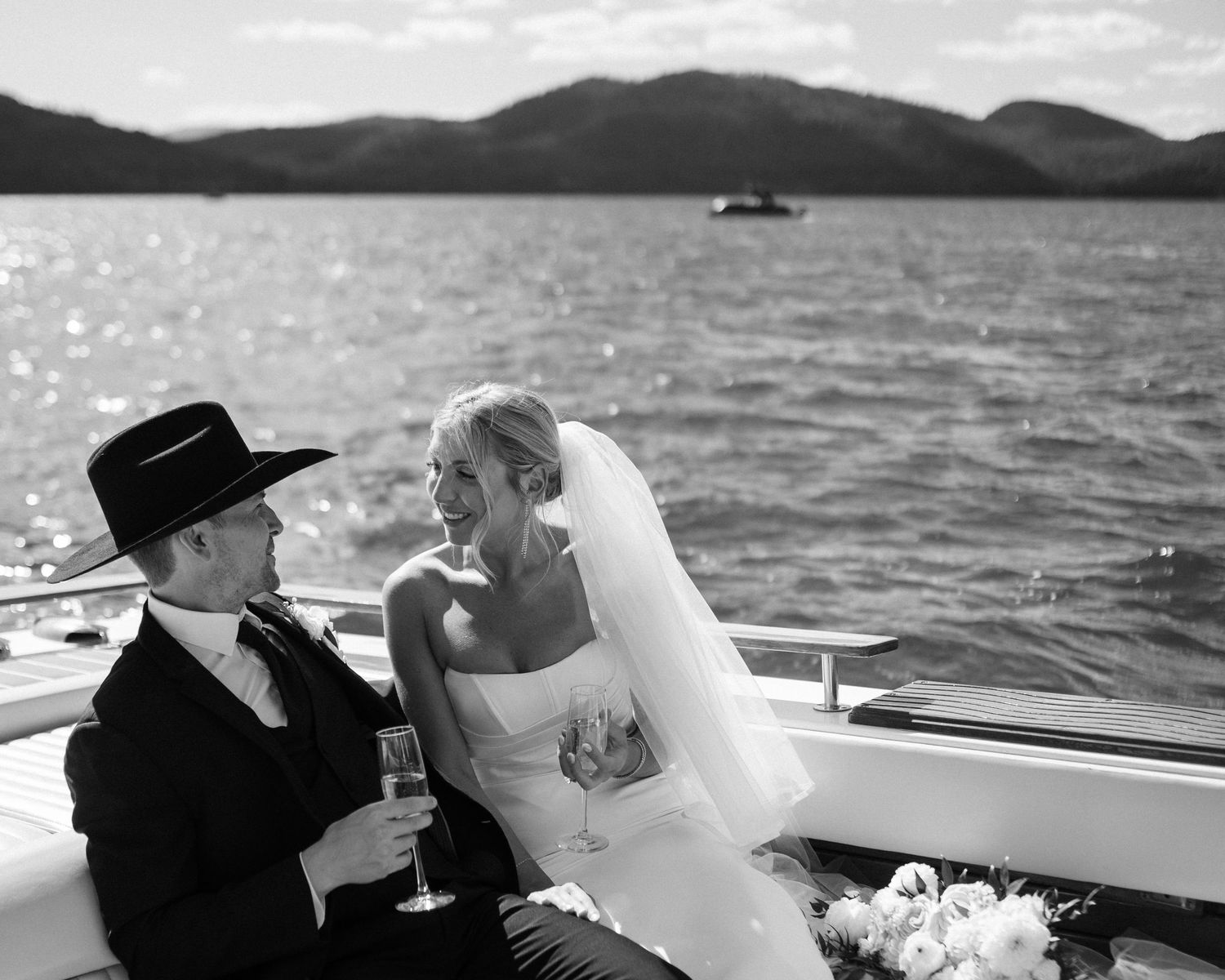 Black and white photo of a couple sharing an intimate moment on a boat with mountain scenery.