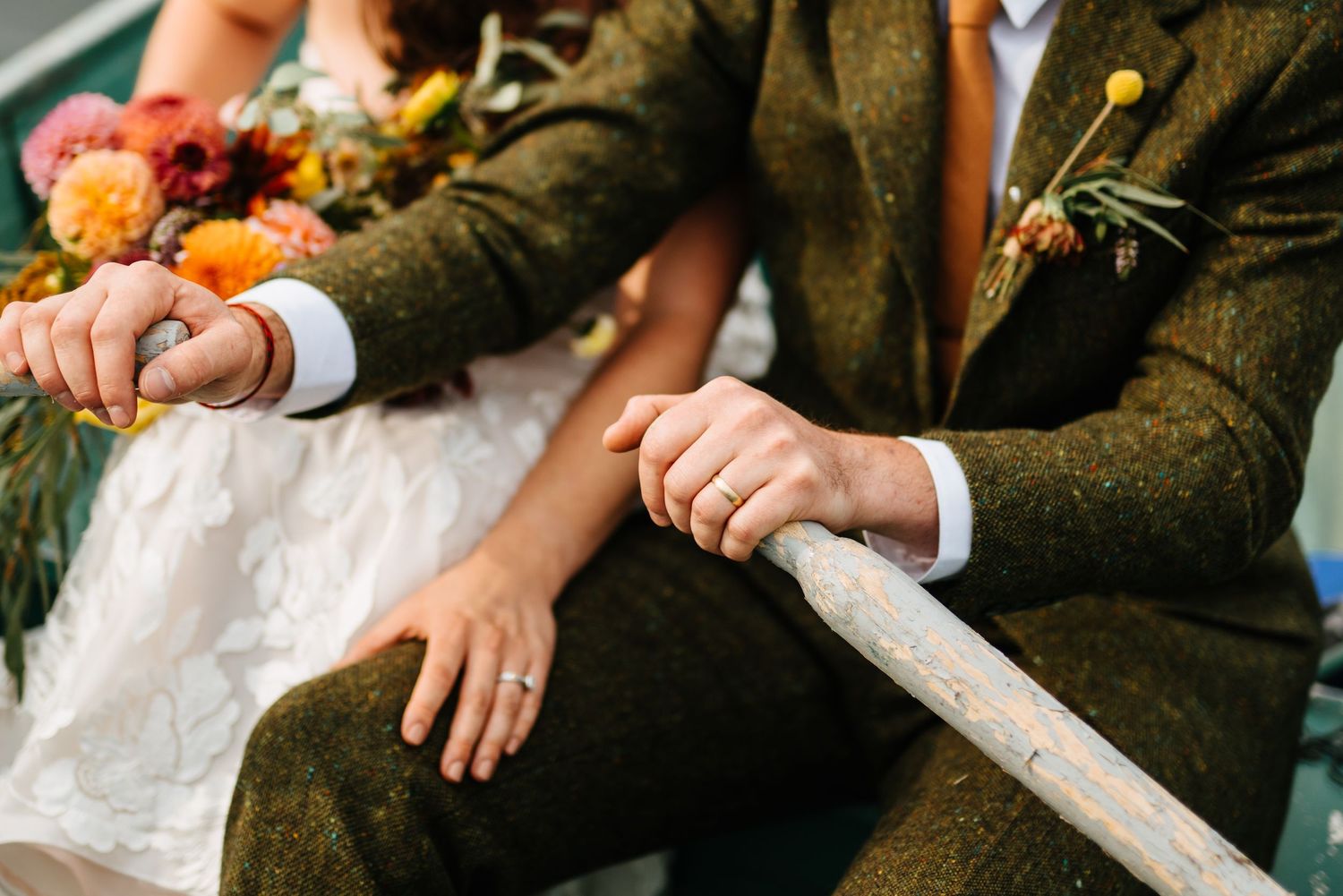 Close-up shot of hands holding a bouquet of orange and pink flowers against a brown tweed jacket.