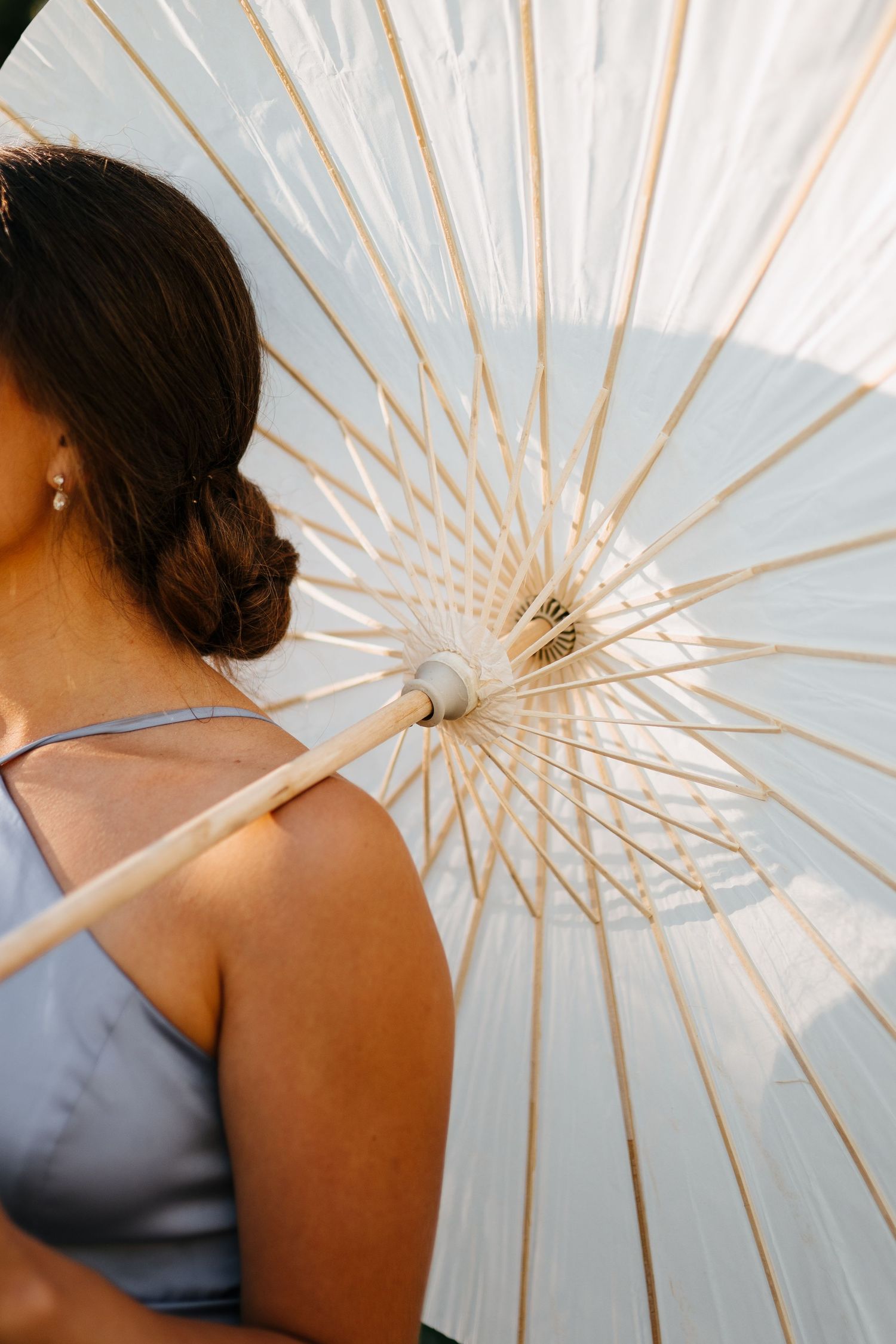 Artistic close-up of a white paper parasol with geometric patterns and a shoulder in soft lighting.