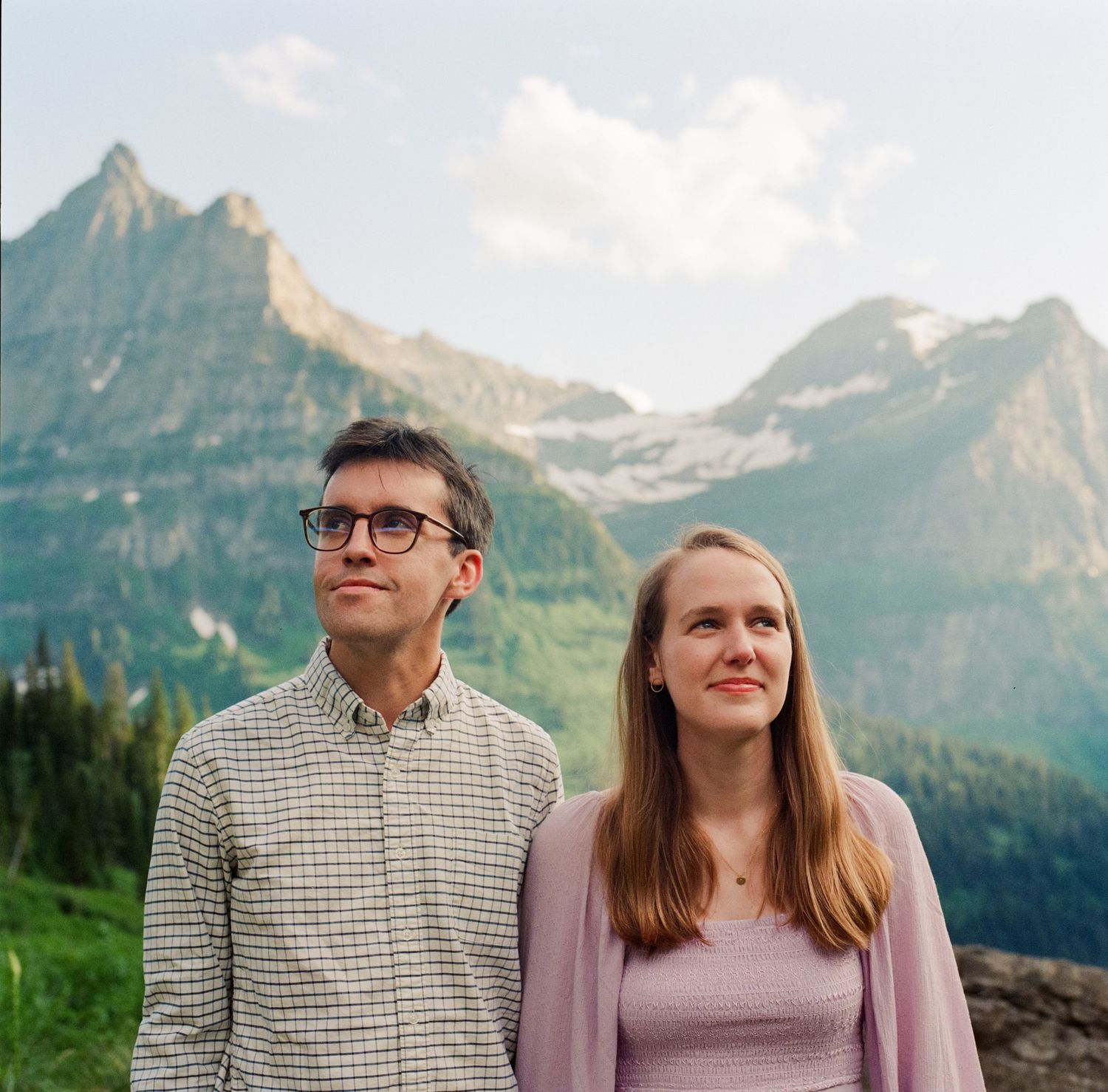 A couple poses together with stunning mountain peaks and lush green slopes in the background.