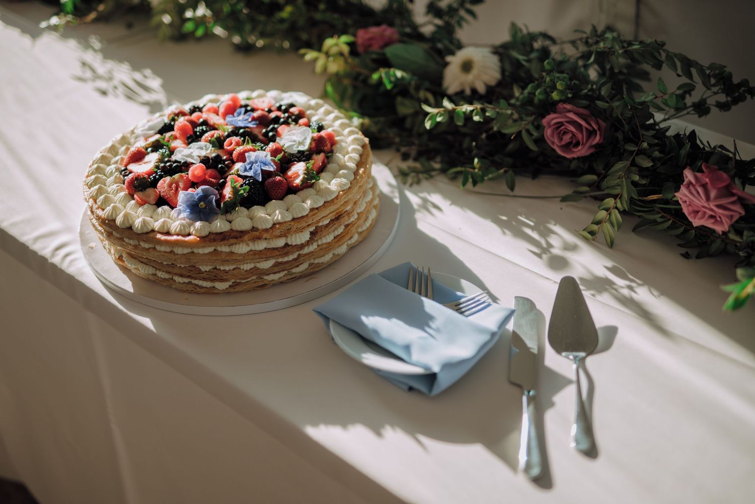 A rustic wedding cake decorated with fresh berries and flowers sits on an elegant white tablecloth.