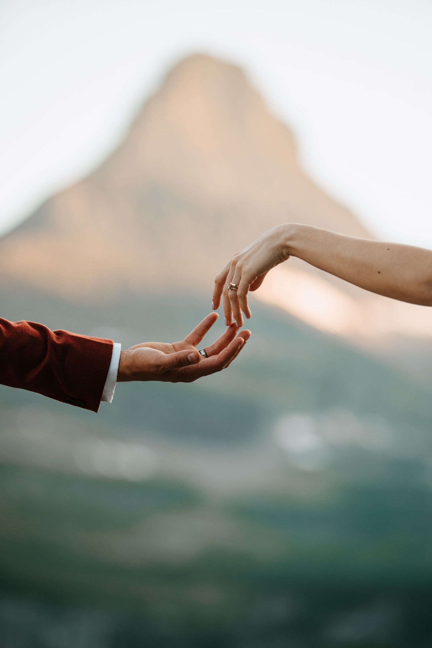 Two hands reaching towards each other with mountain silhouette in background.