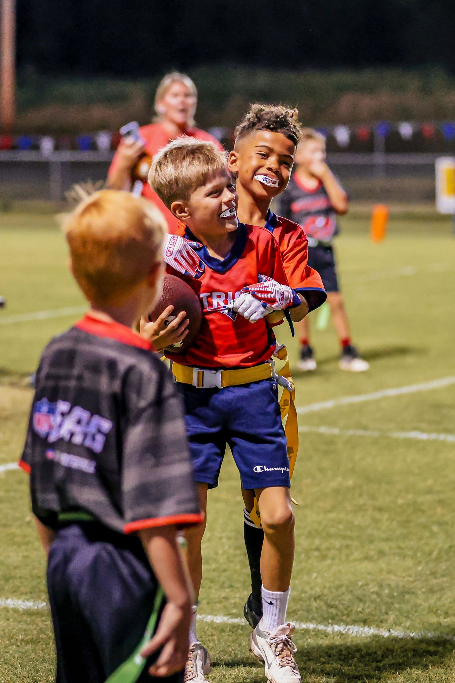 Young athletes in sports uniforms share joyful moments on a football field during evening practice.